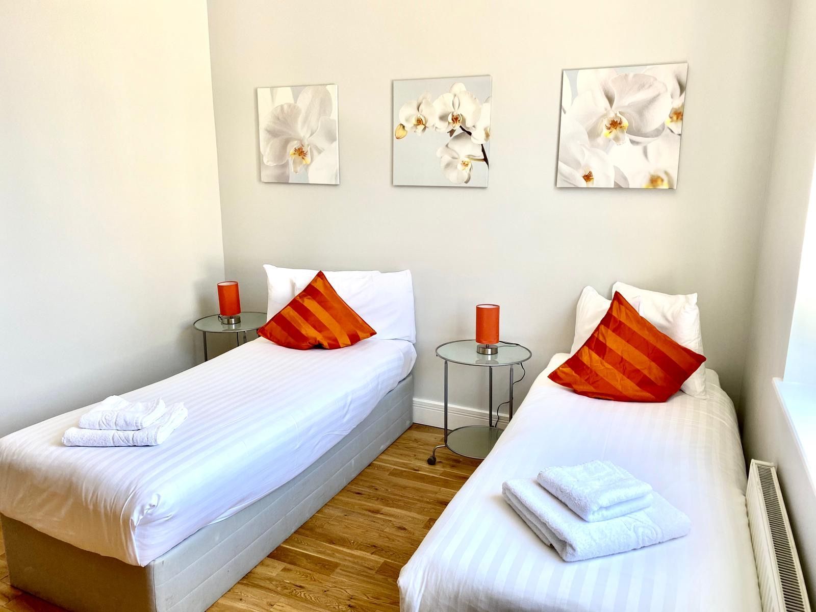 A bedroom with two beds and three paintings on the wall
