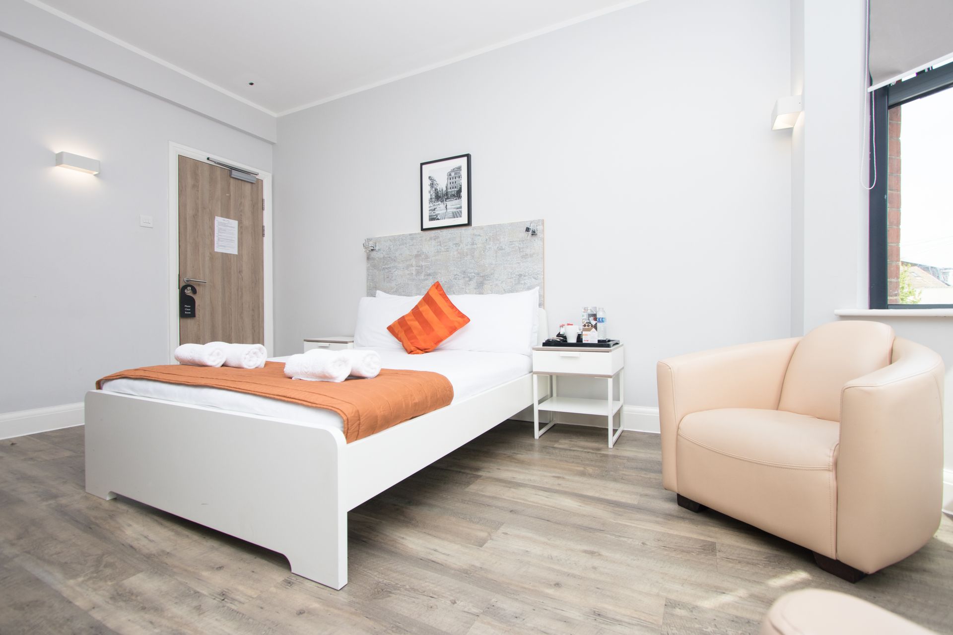 A hotel room with a bed , chair , nightstand and window.