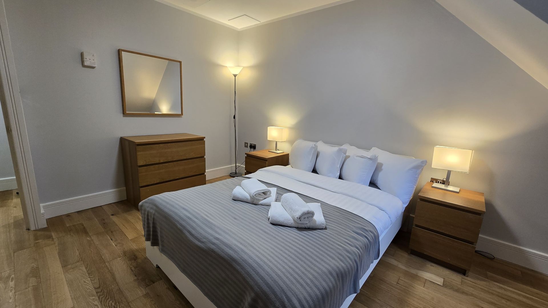 A bedroom with a bed , nightstands , dresser and mirror.