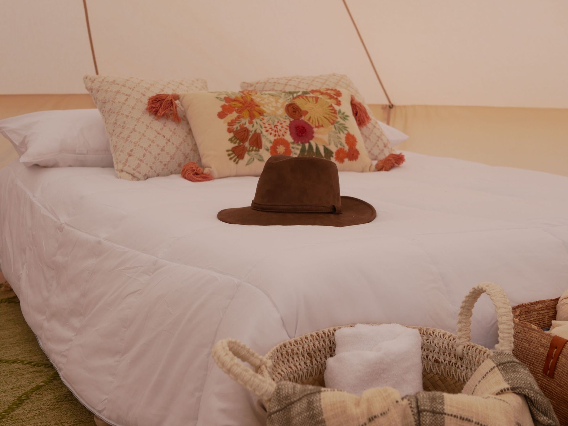 Una cama con un sombrero, almohadas y una cesta de toallas encima.