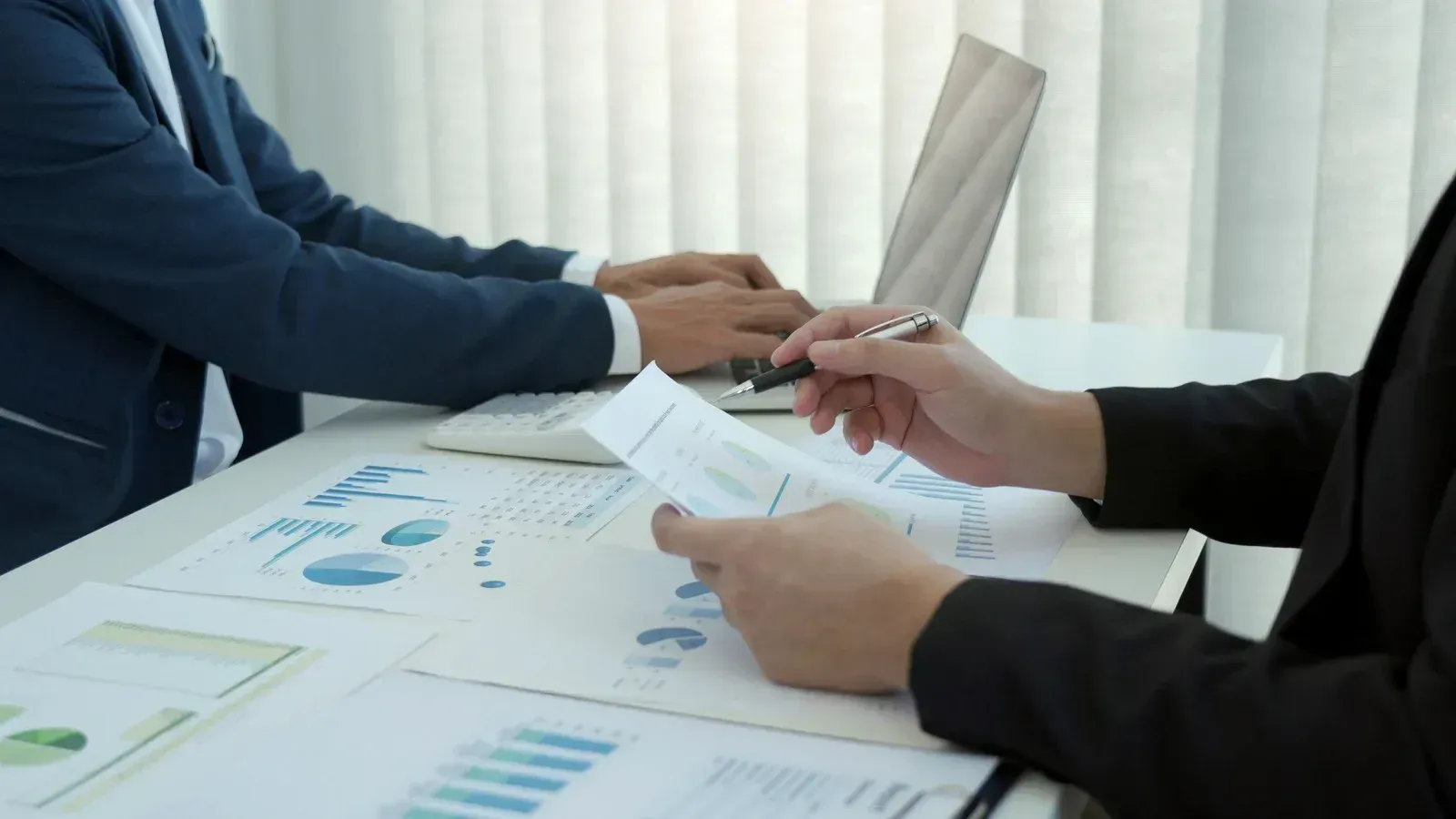 Two people in business attire reviewing charts and documents at a desk during a meeting