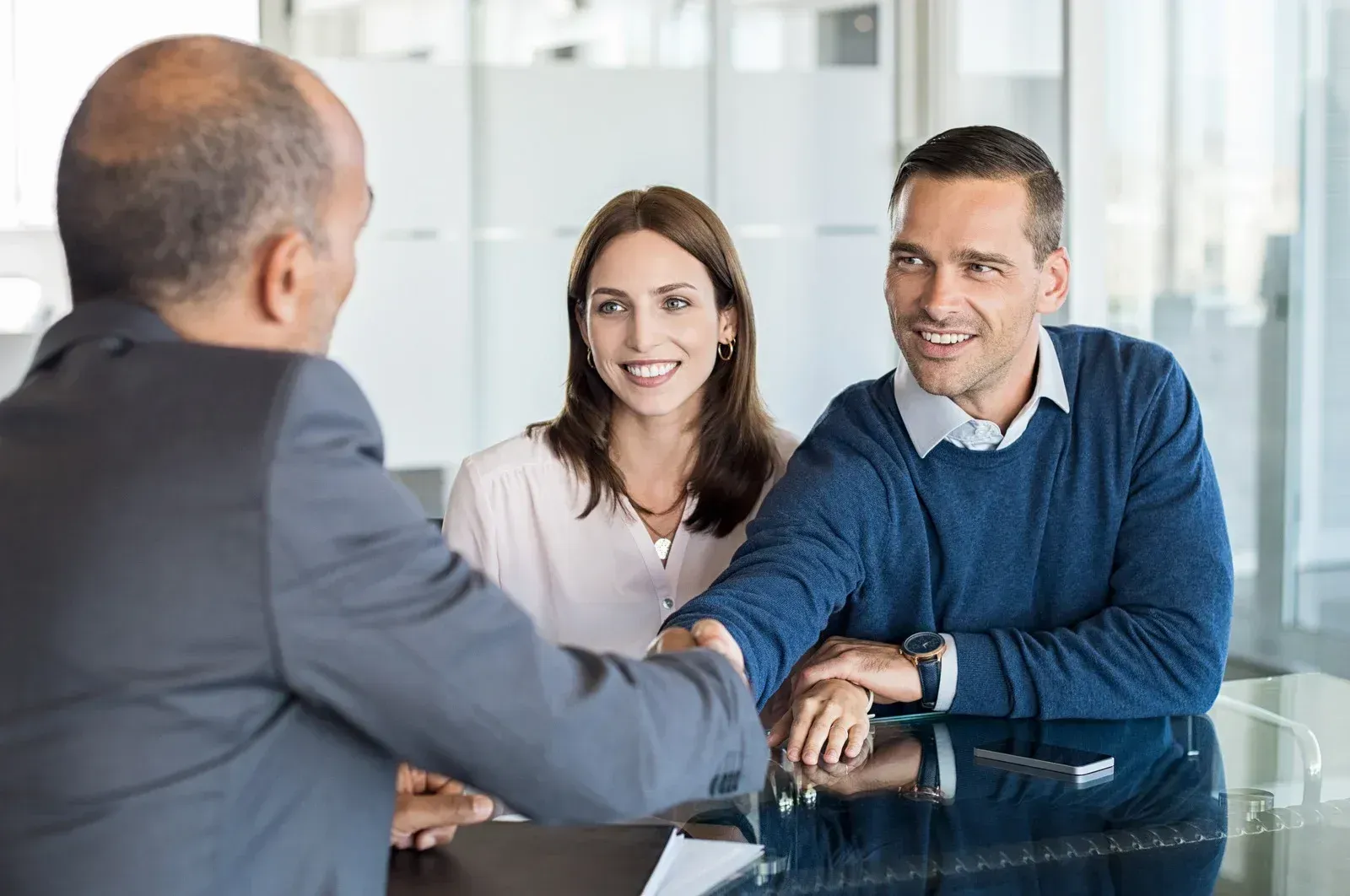 Business meeting with three people shaking hands across a glass table in a bright office