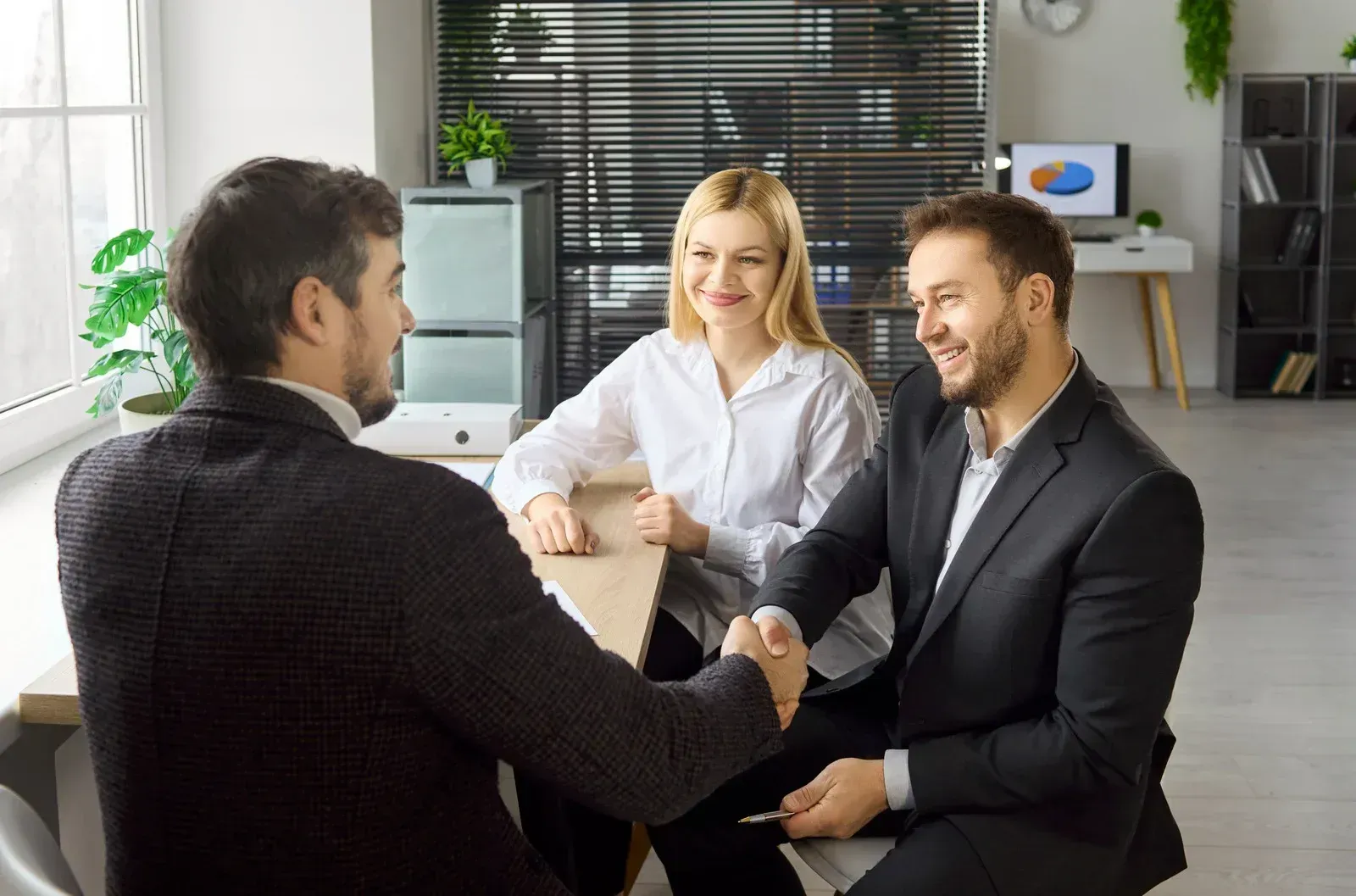 Three businesspeople shaking hands in a bright office, smiling during a meeting