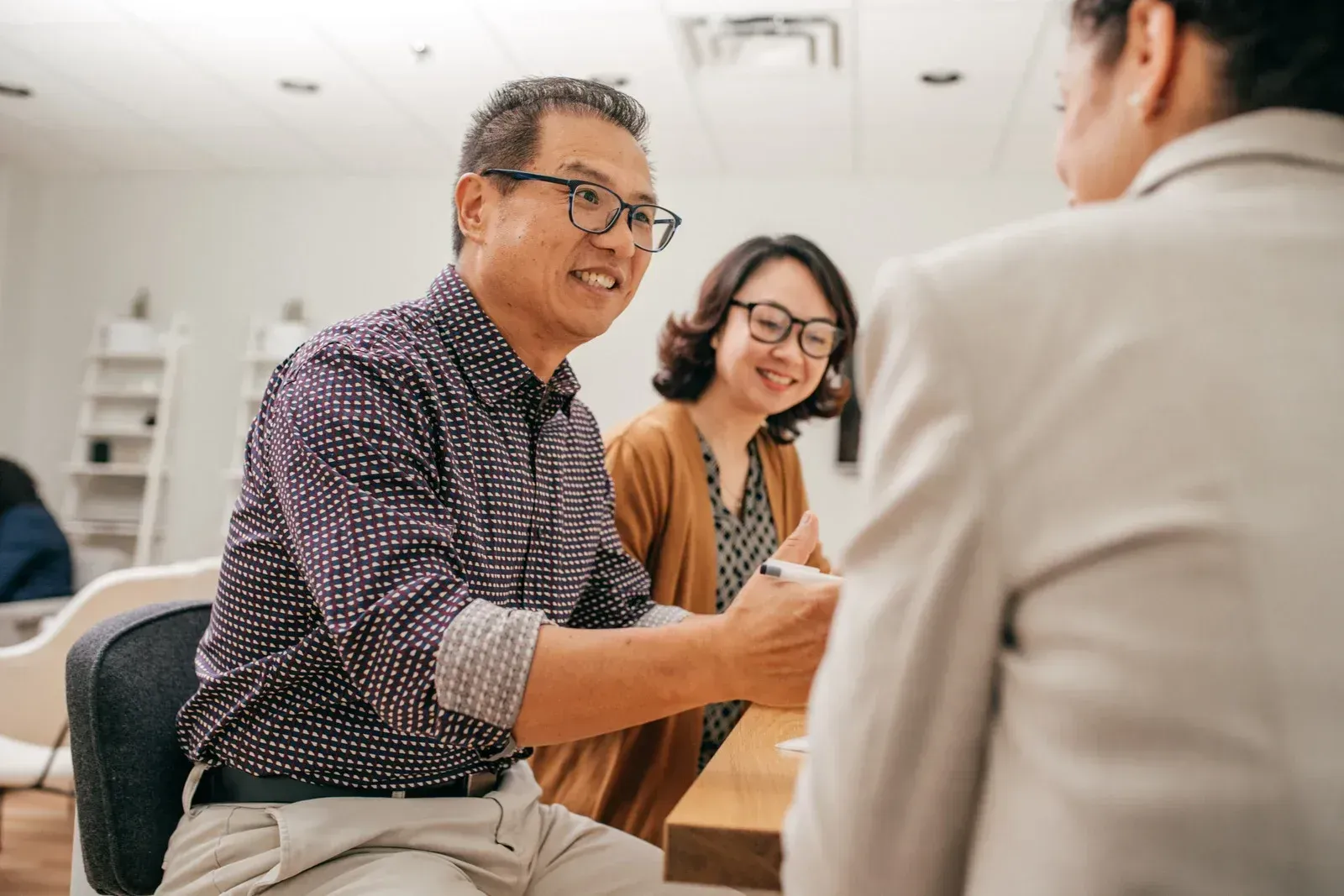 Three people in a bright office, smiling and talking during a meeting.