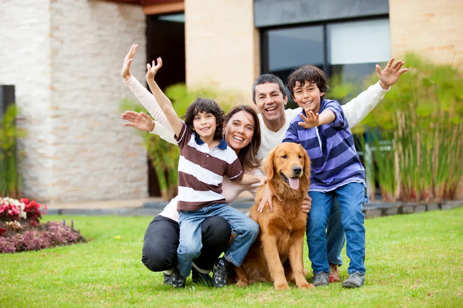 Family with a golden retriever smiling and waving on a lawn in front of a house