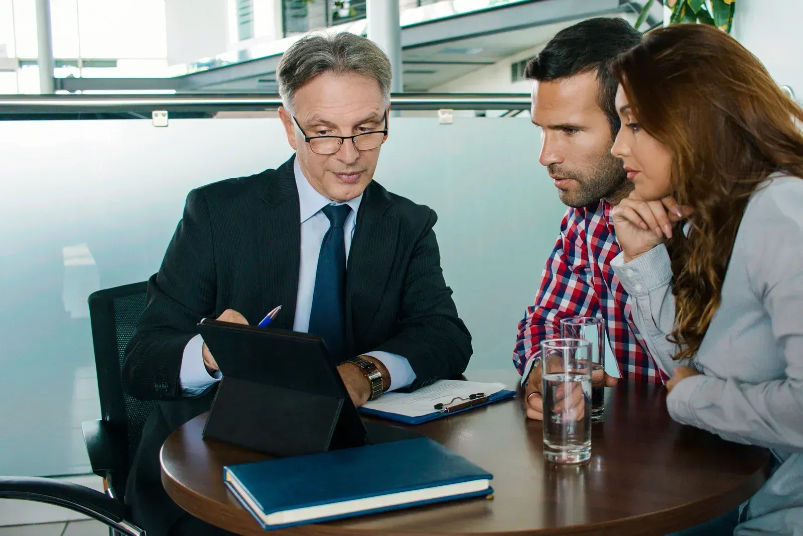 Three people reviewing documents at a table in a bright office meeting room