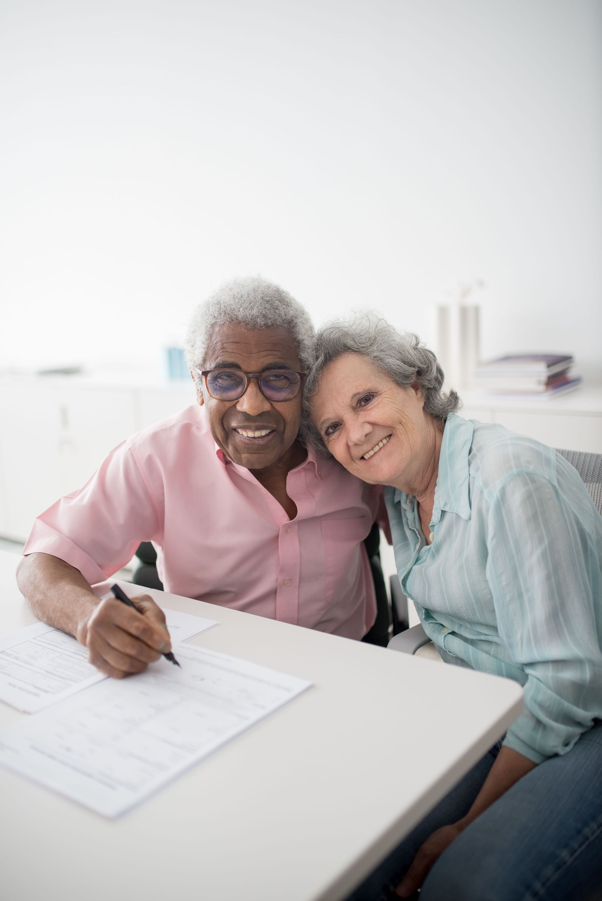 Two people smiling at a table, one signing paperwork while seated in a bright office