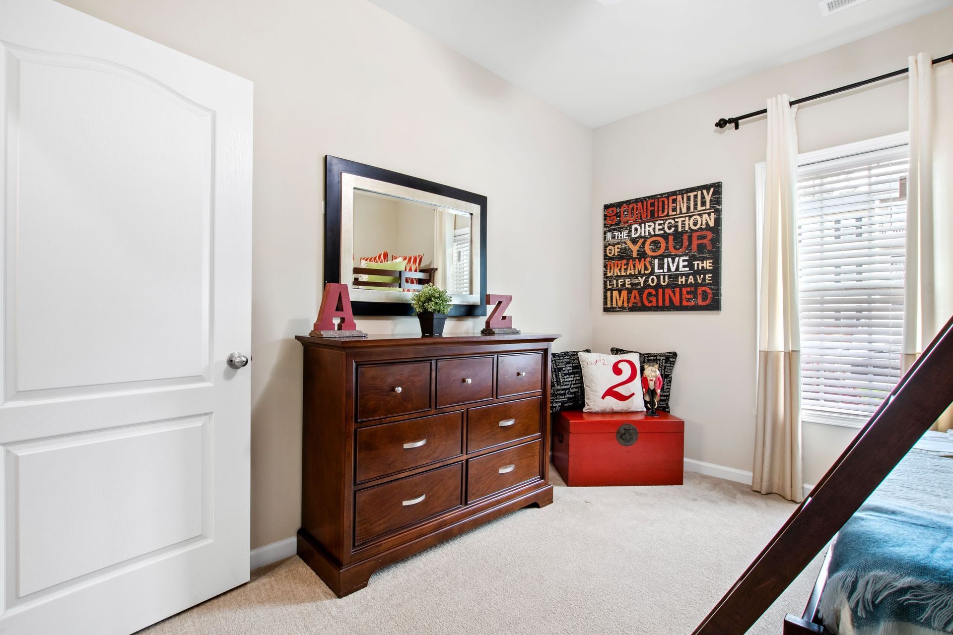 Bedroom in an apartment with a dark wood dresser, mirror, and window with light curtains.