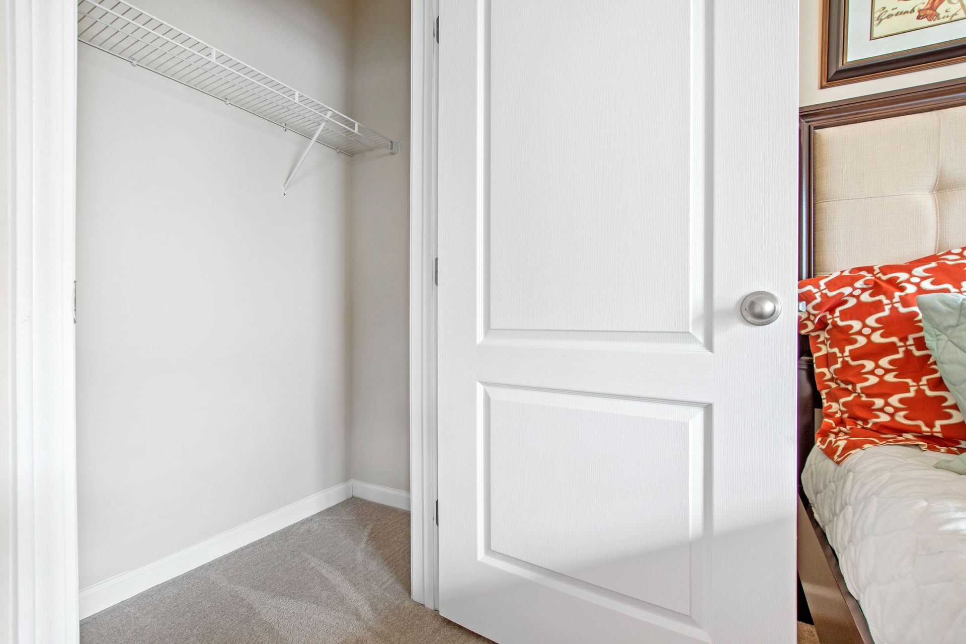Open closet with a wire shelf in a bedroom; white door and beige carpet visible.