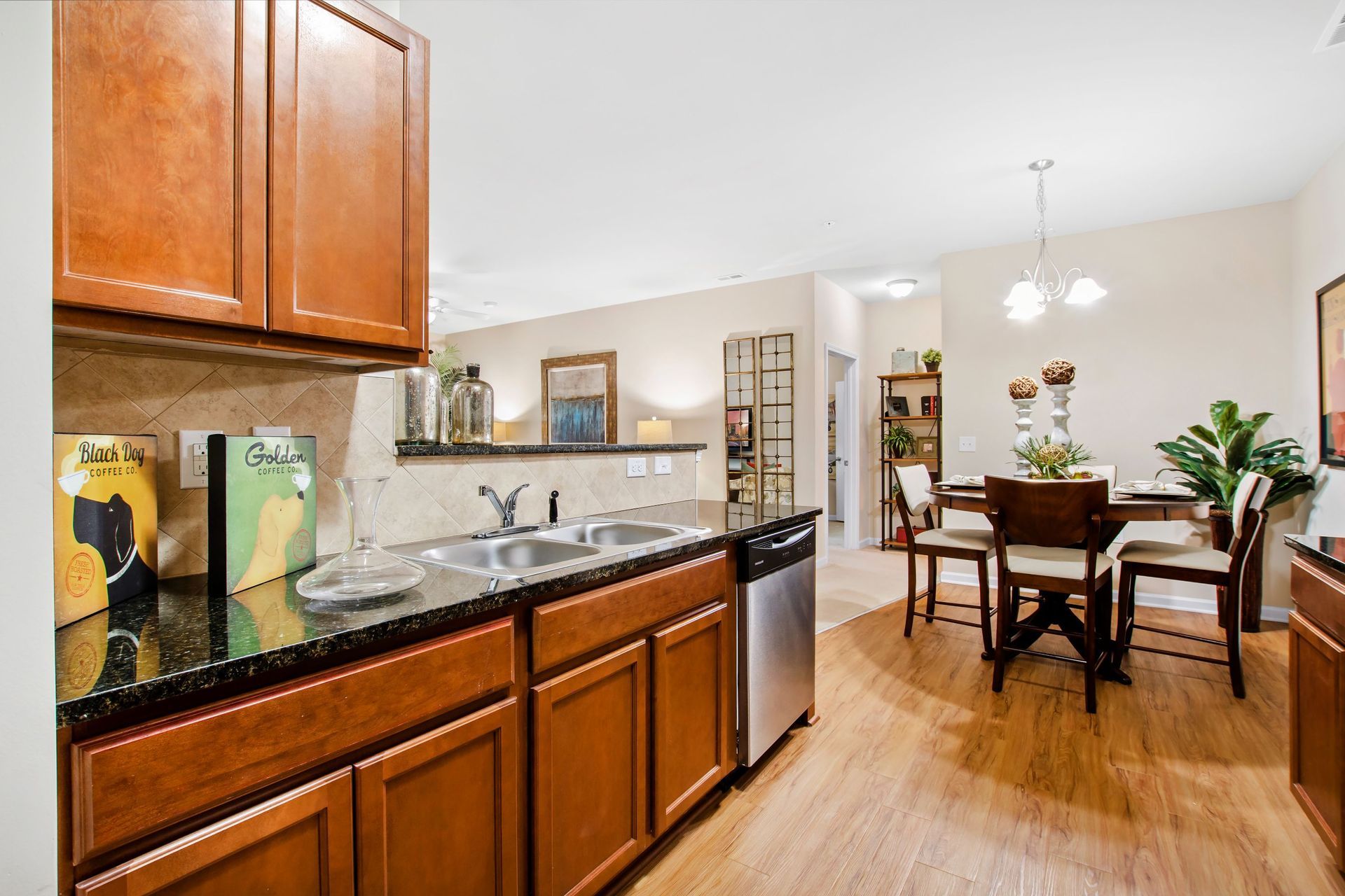 Open-concept kitchen with brown wood cabinets, granite counters, double sink, and a nearby dining area.