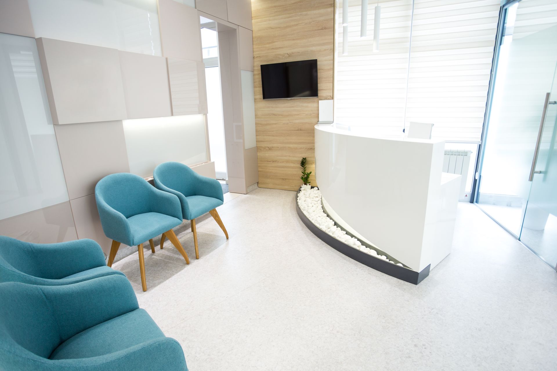 Waiting room with blue chairs, white reception desk, and TV.