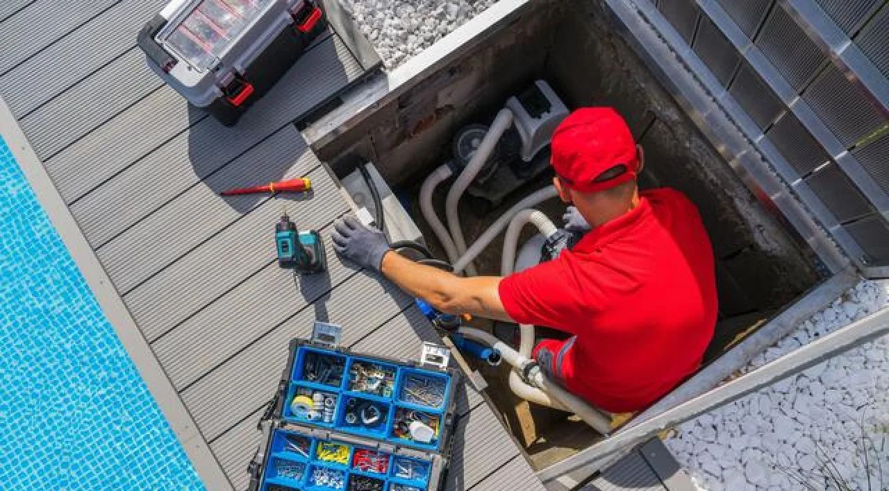 Plumber in red uniform working in an open floor drain with pipes and tools in a utility area