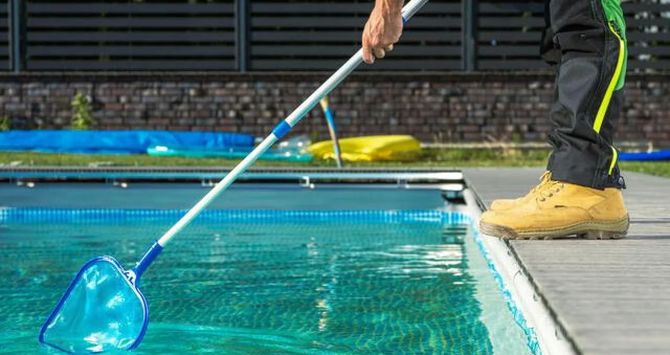 Person skimming a swimming pool with a blue net beside the deck