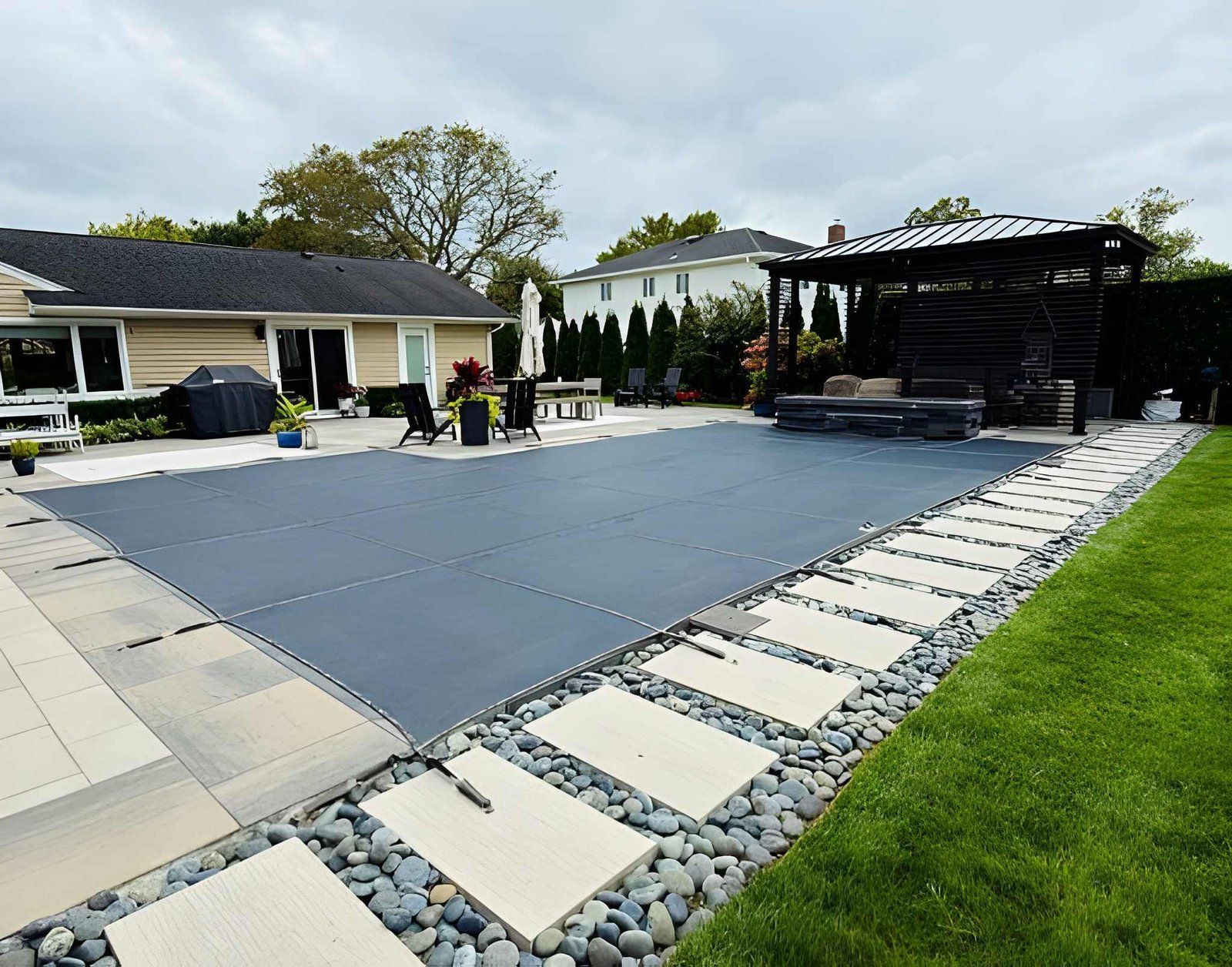 Backyard patio with a large blue pool cover, stepping stones, and a covered outdoor seating area