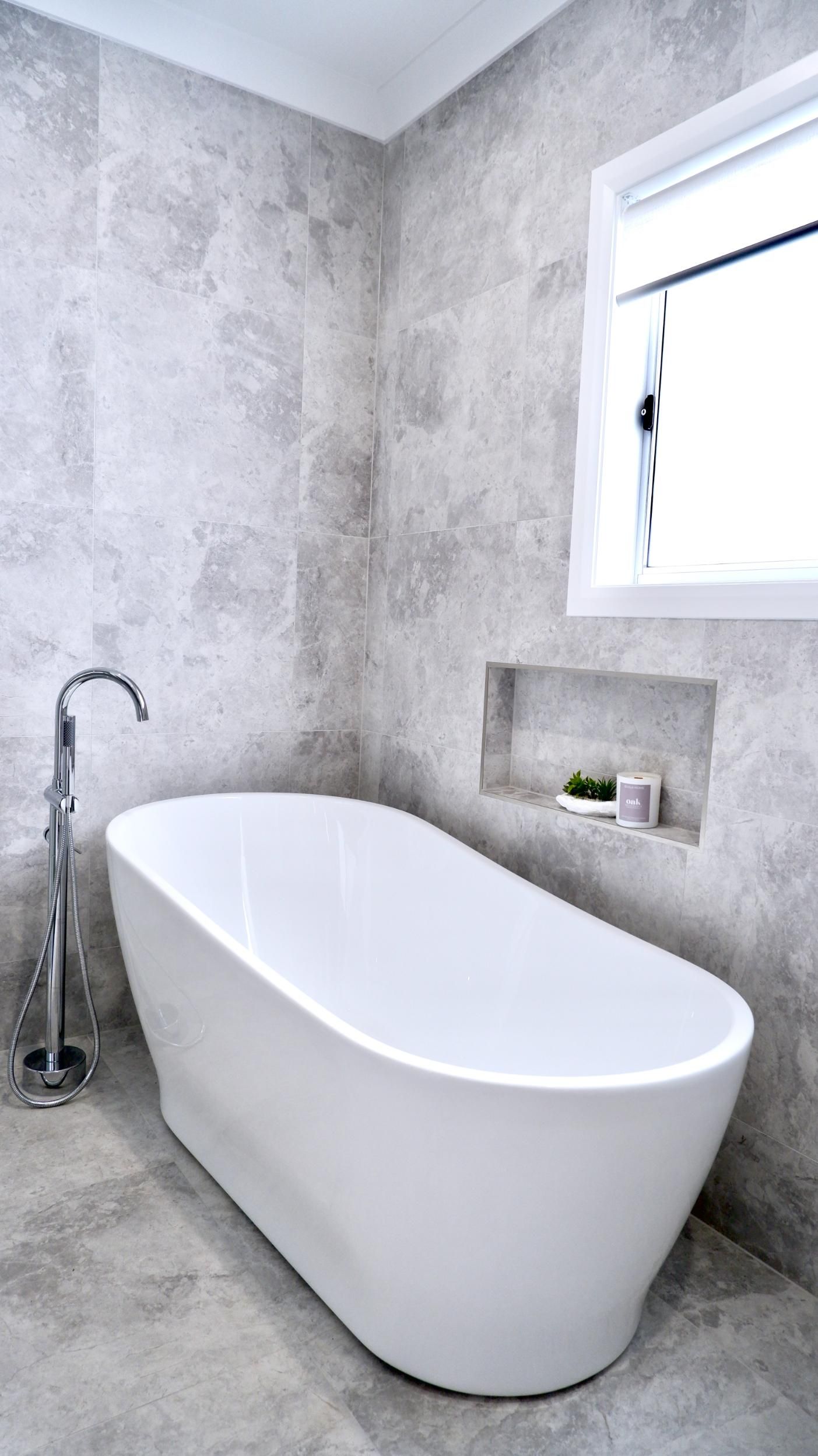 A white bathtub is sitting in a bathroom next to a window.