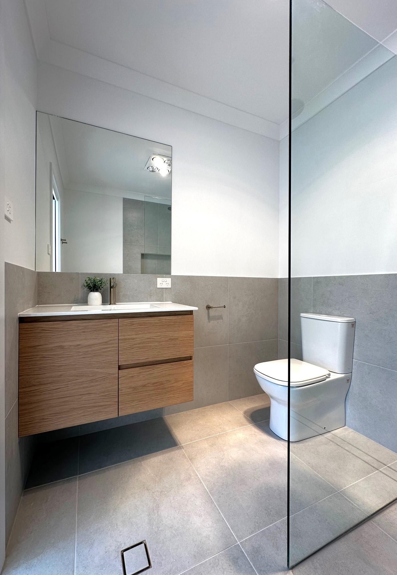 A bathroom with a toilet , sink , mirror and walk in shower.