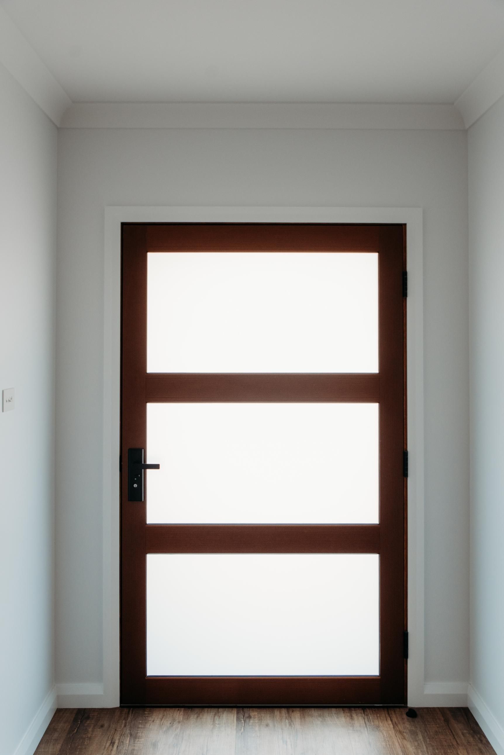 A wooden door with three windows in a hallway.