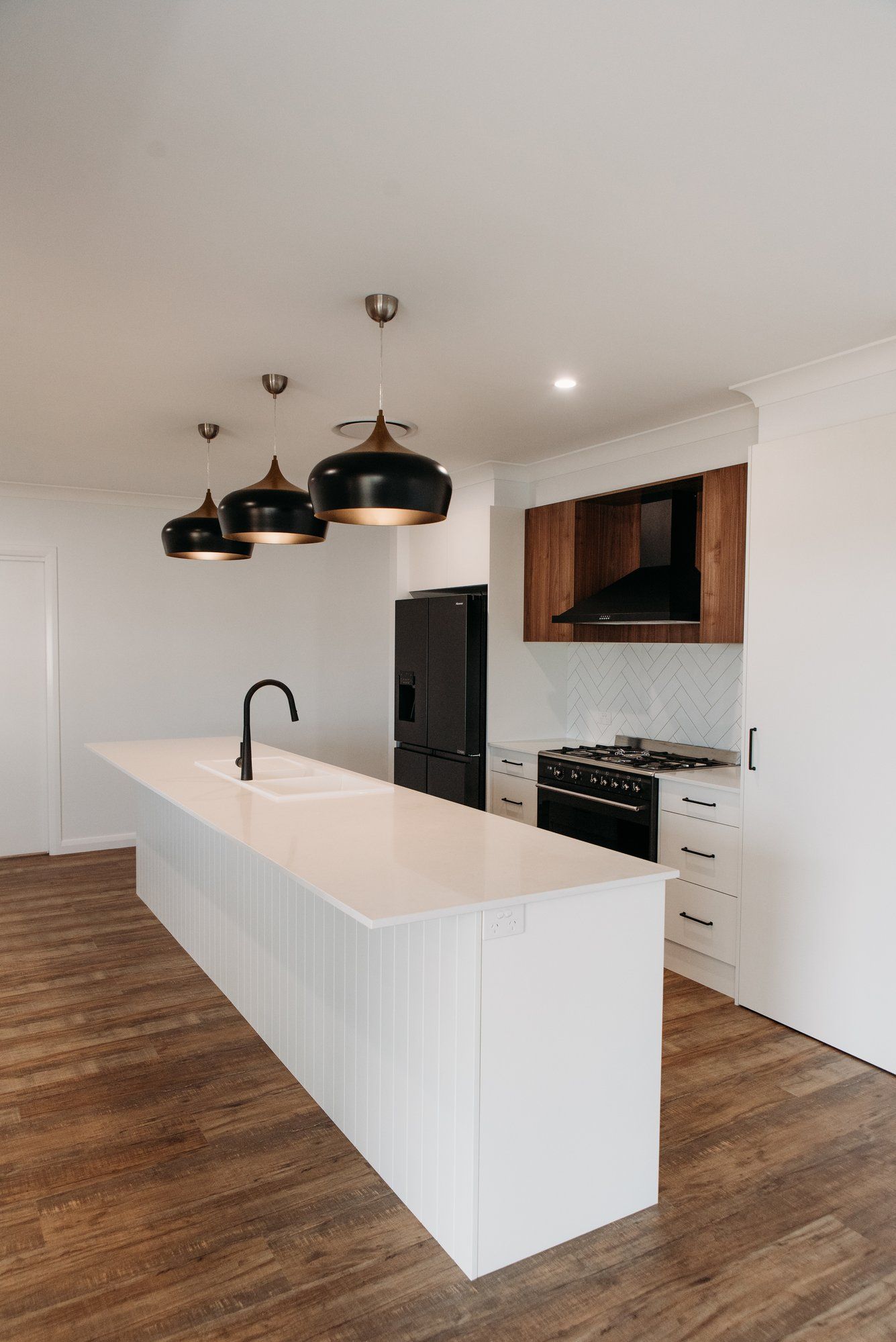 A kitchen with a long island , a refrigerator , a stove , and a sink.