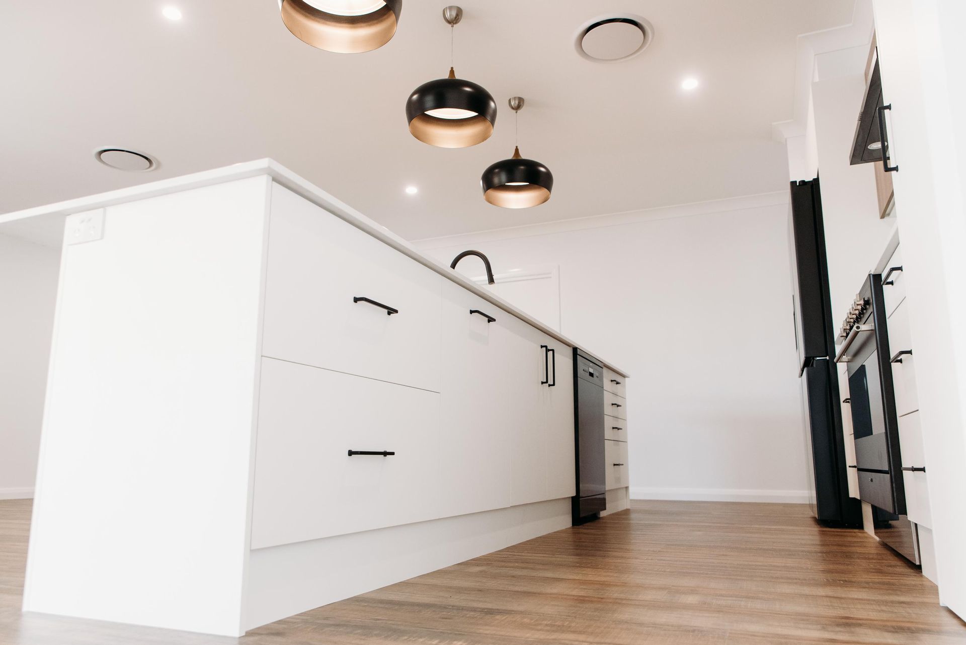 An empty kitchen with white cabinets and a wooden floor.