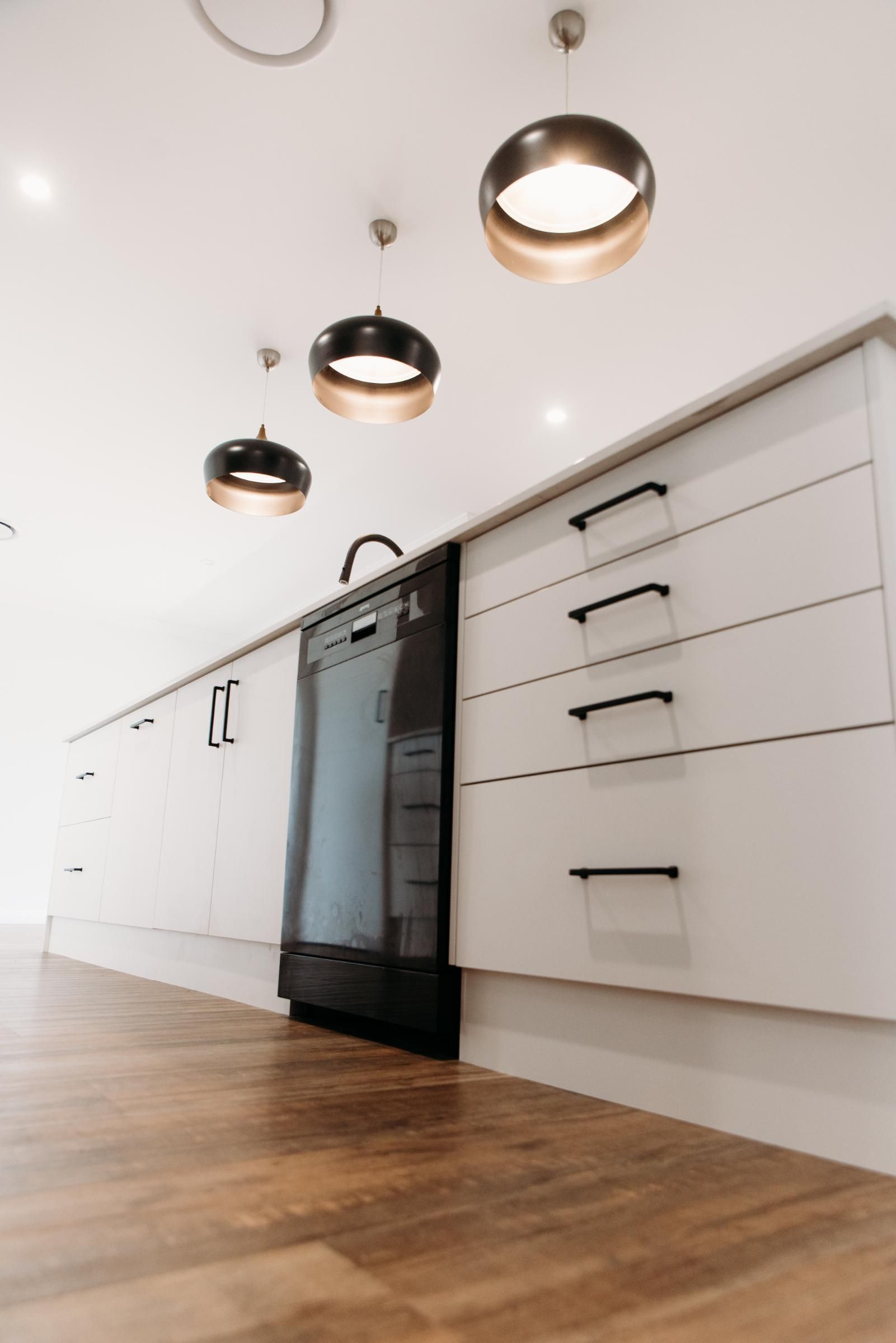 A kitchen with white cabinets and black handles and a dishwasher.