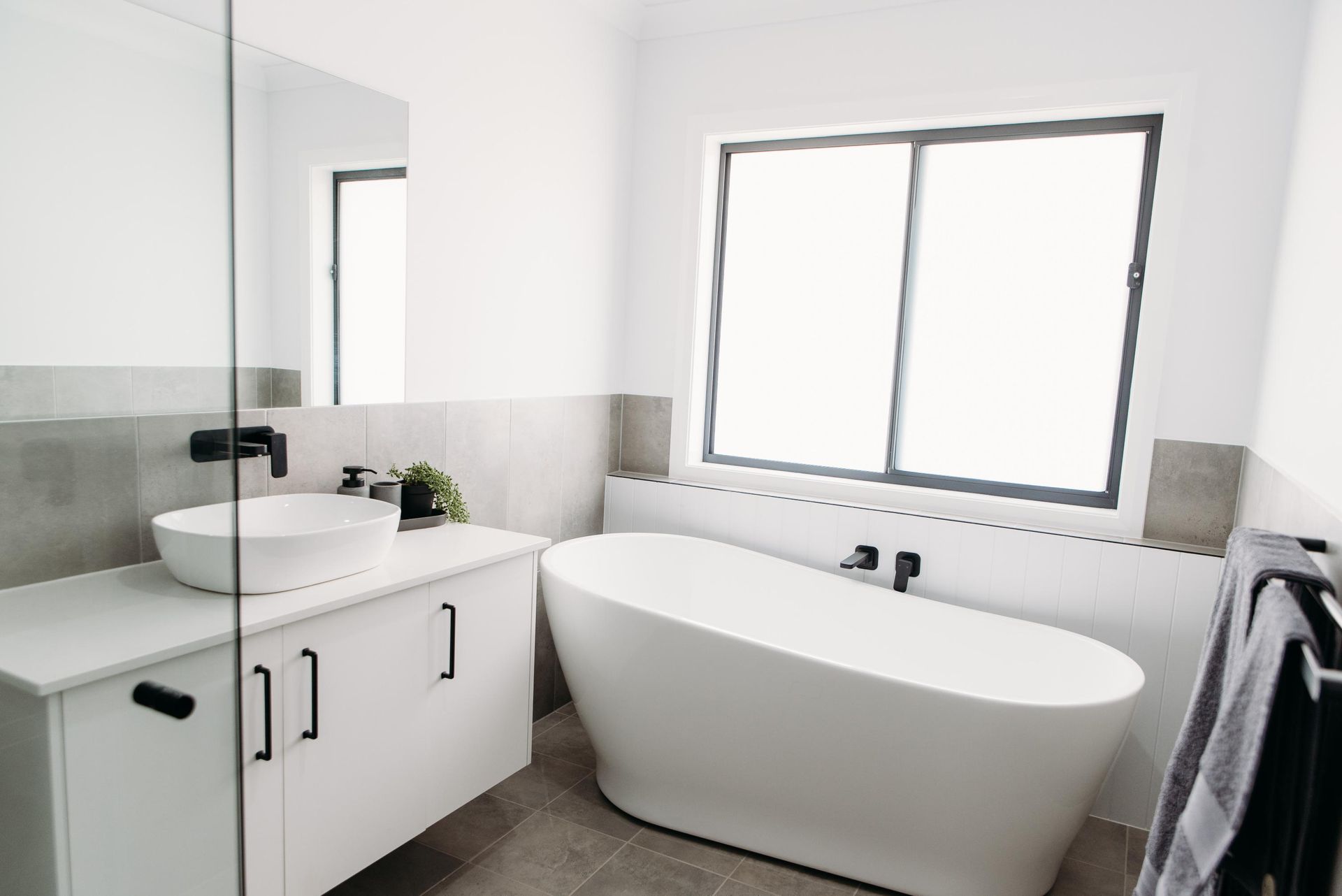 A bathroom with a bathtub , sink , mirror and window.