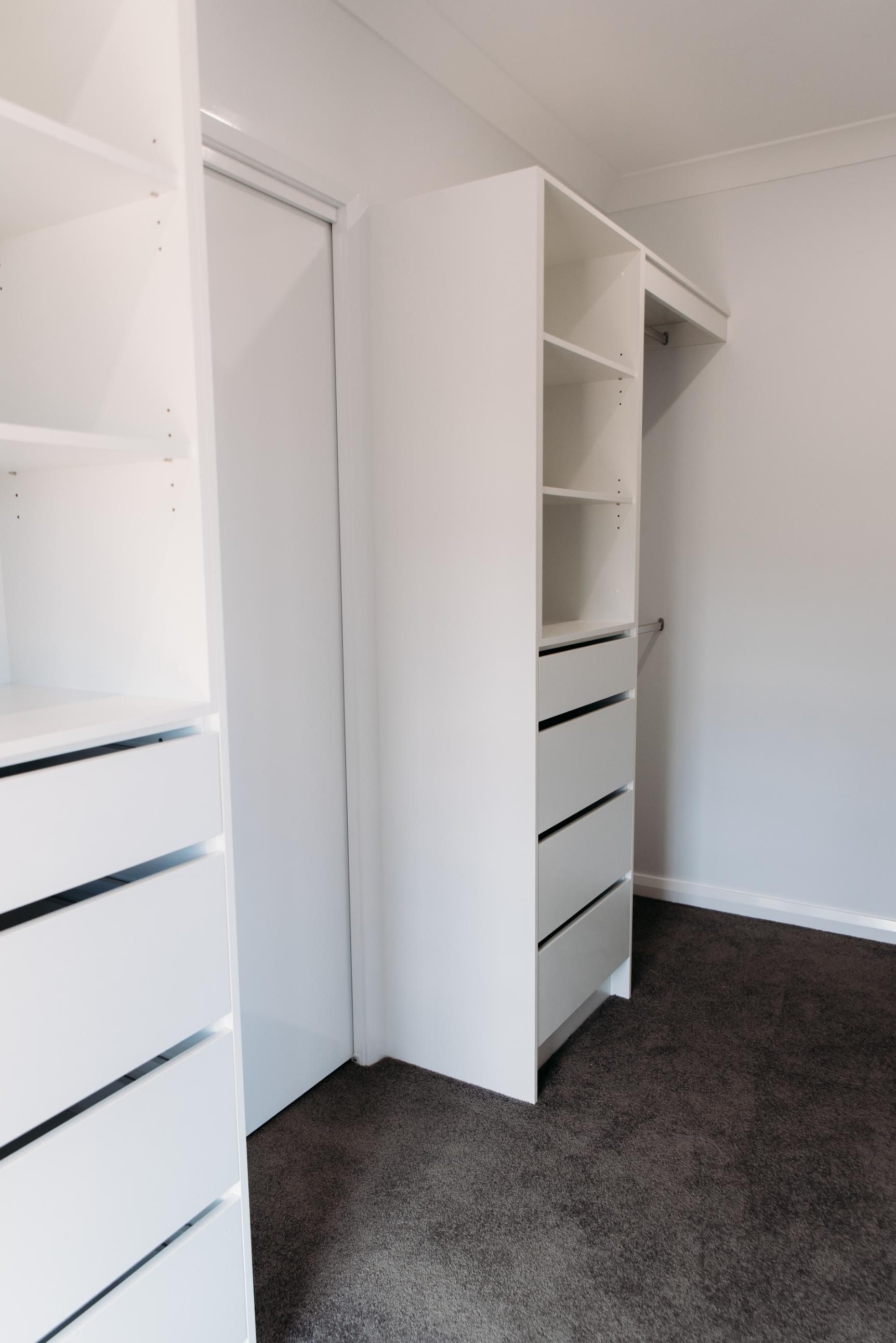 A walk in closet with white shelves and drawers in a bedroom.