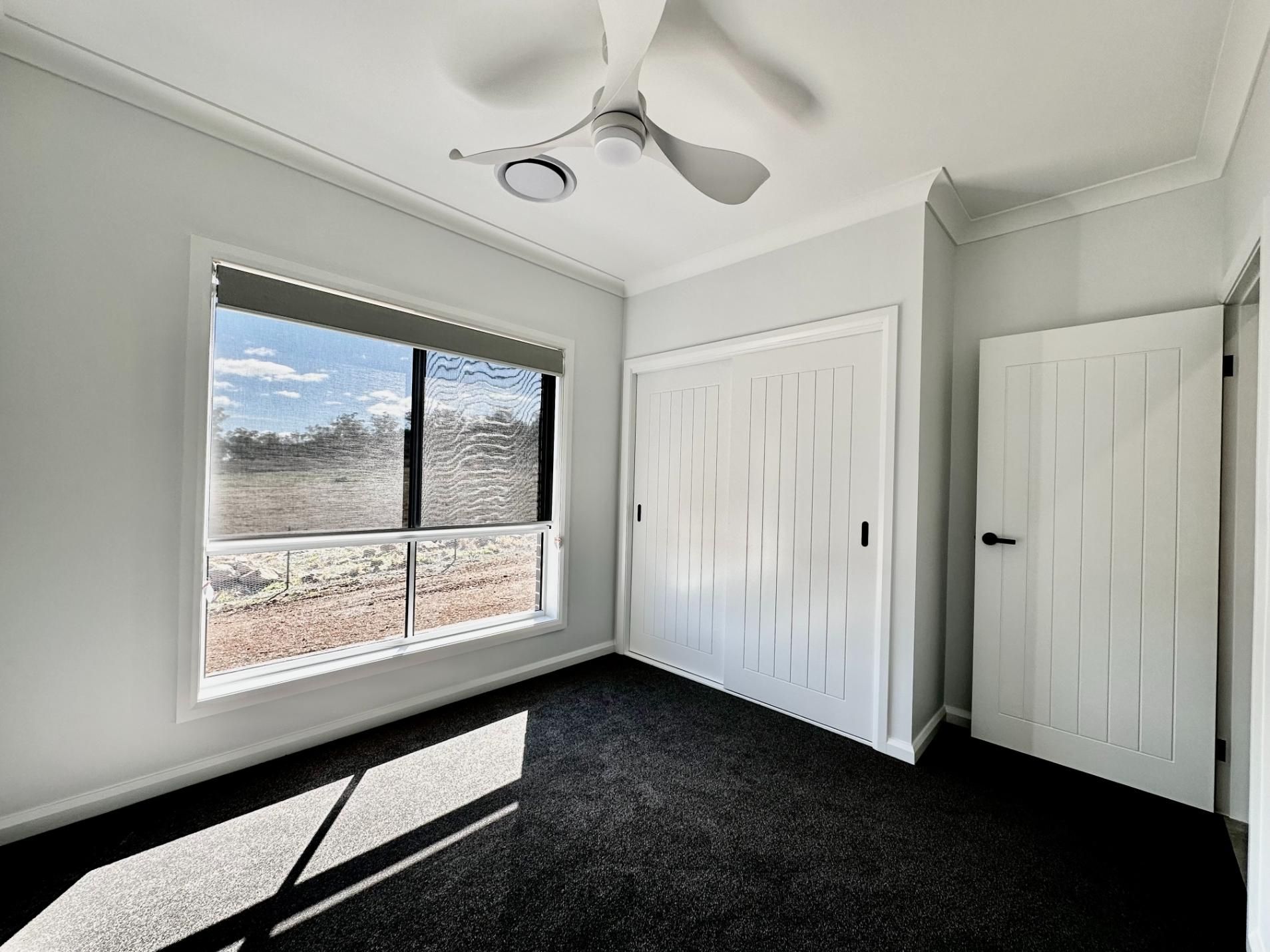 An empty bedroom with a ceiling fan and a window.