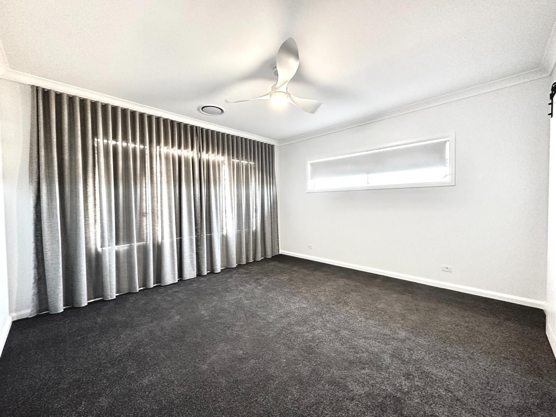 An empty living room with a ceiling fan and curtains.