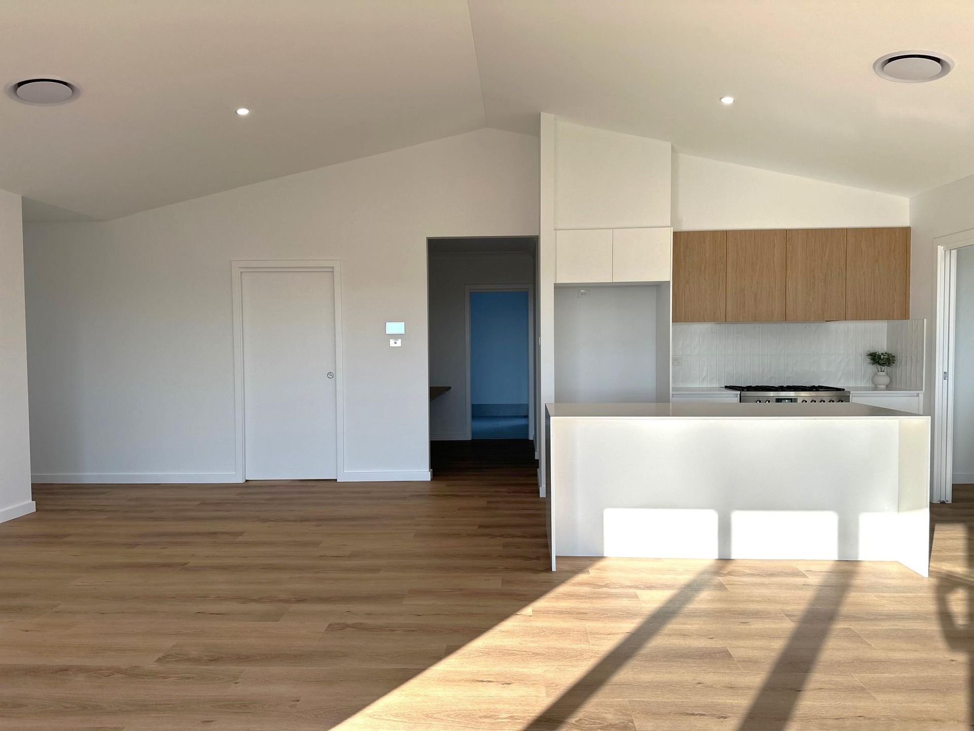 An empty kitchen with wooden floors and white cabinets