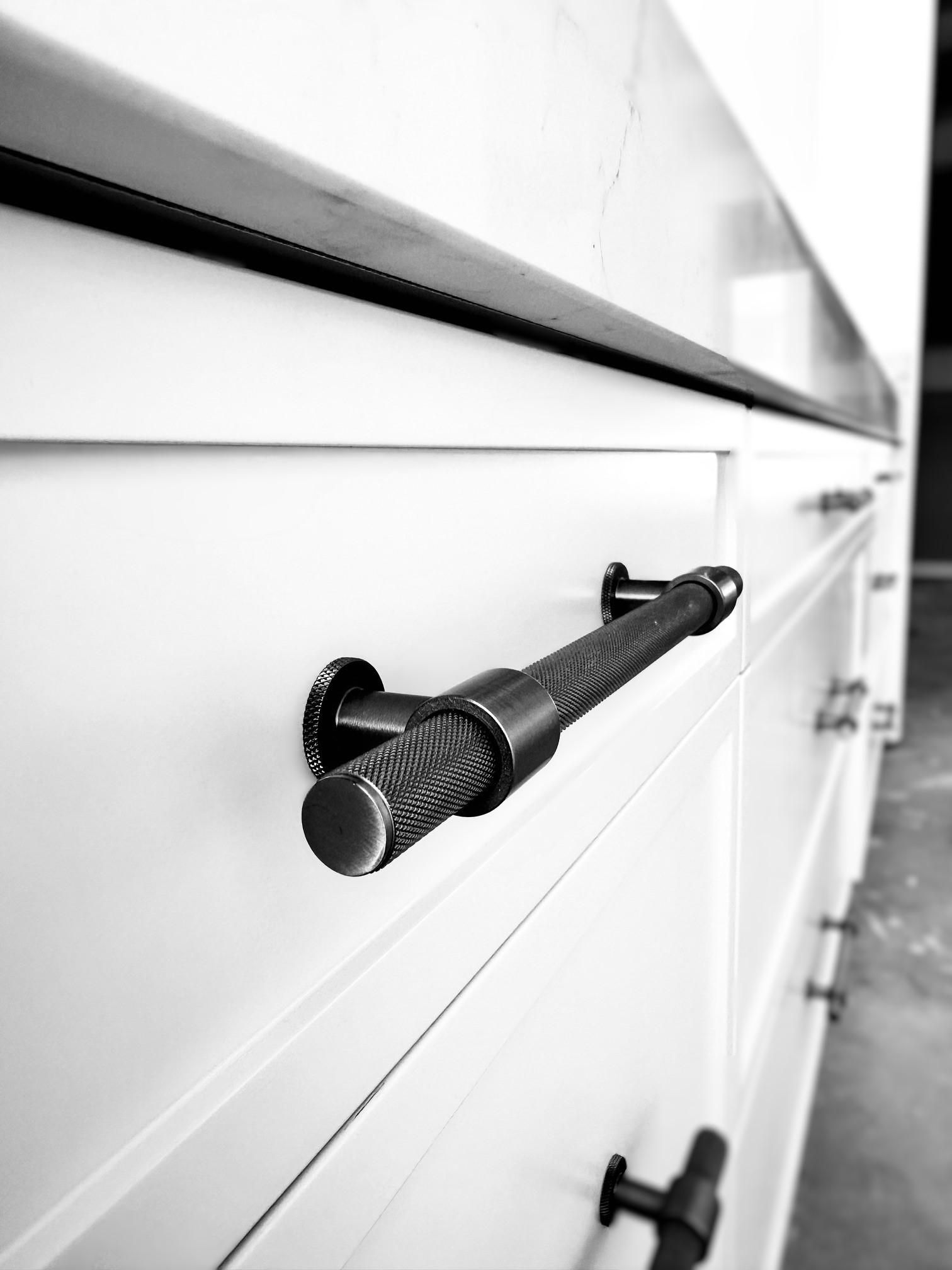 A black and white photo of a black handle on a white cabinet.