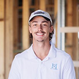 A young man wearing a baseball cap and a white shirt is standing in a field.