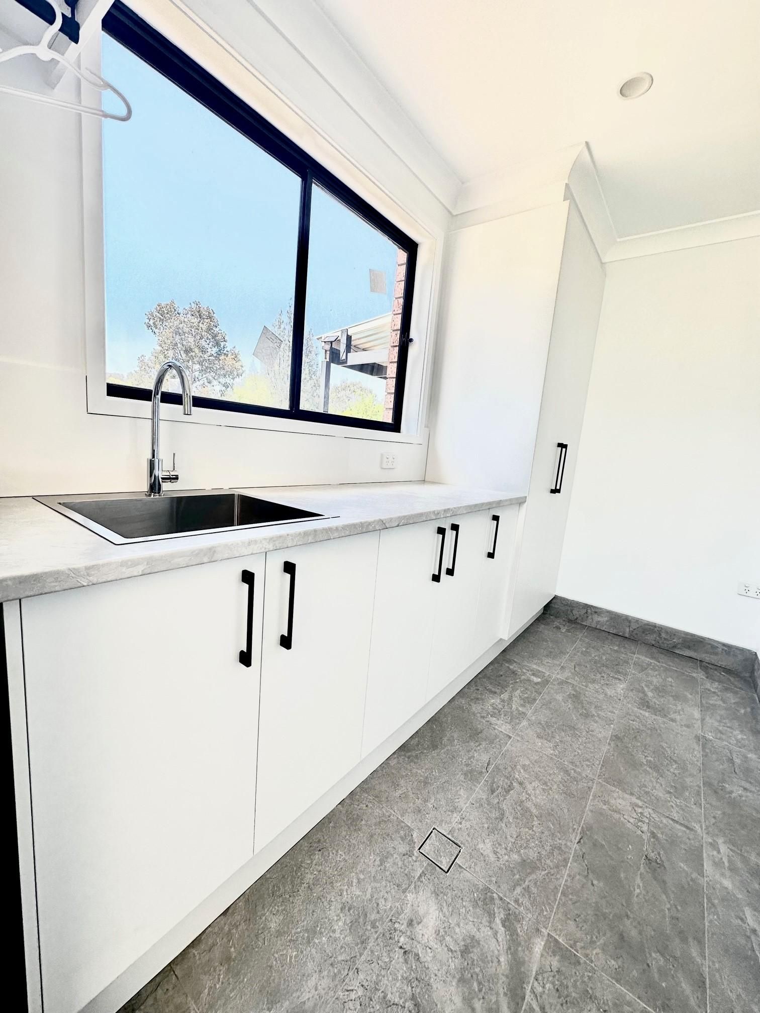 A kitchen with white cabinets , a sink , and a window.