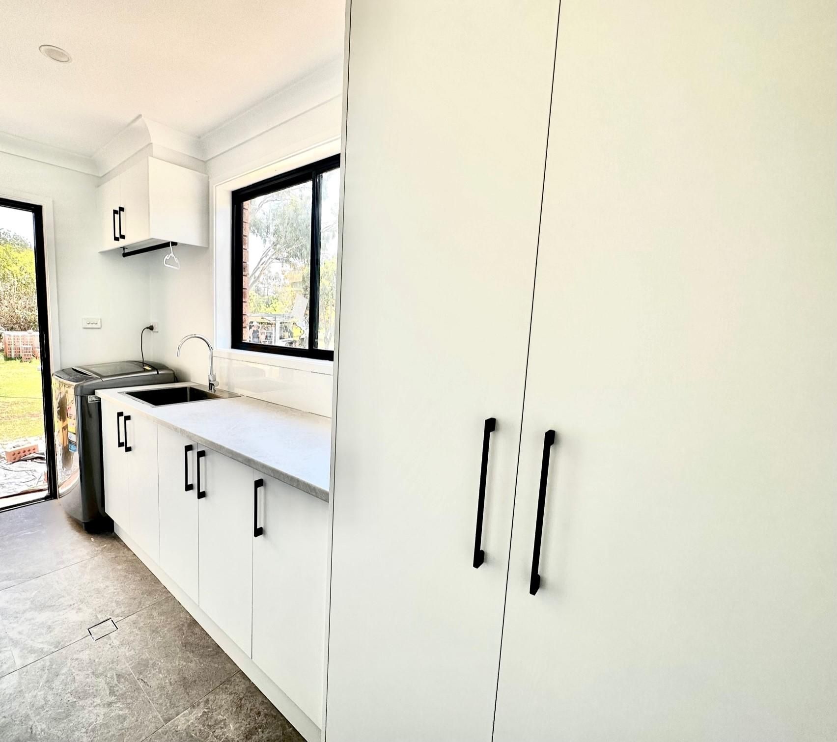 A kitchen with white cabinets , a sink , and a window.