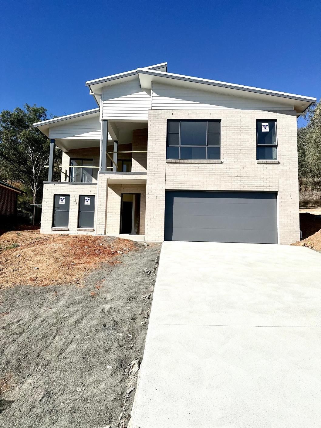 A large white house with a gray garage door is sitting on top of a hill.