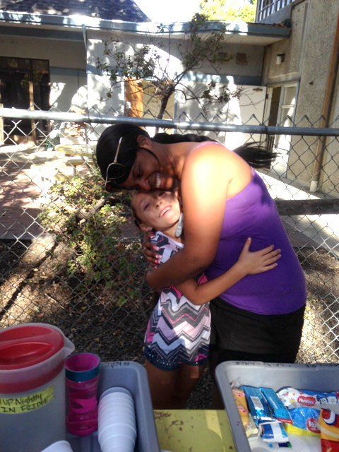 A woman in a purple tank top is hugging a little girl