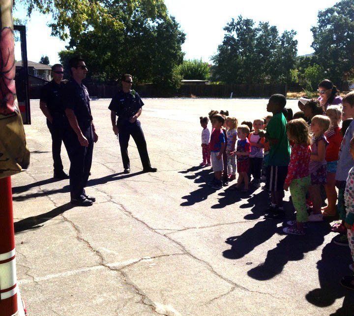 A group of children standing in a parking lot with a fireman in the background