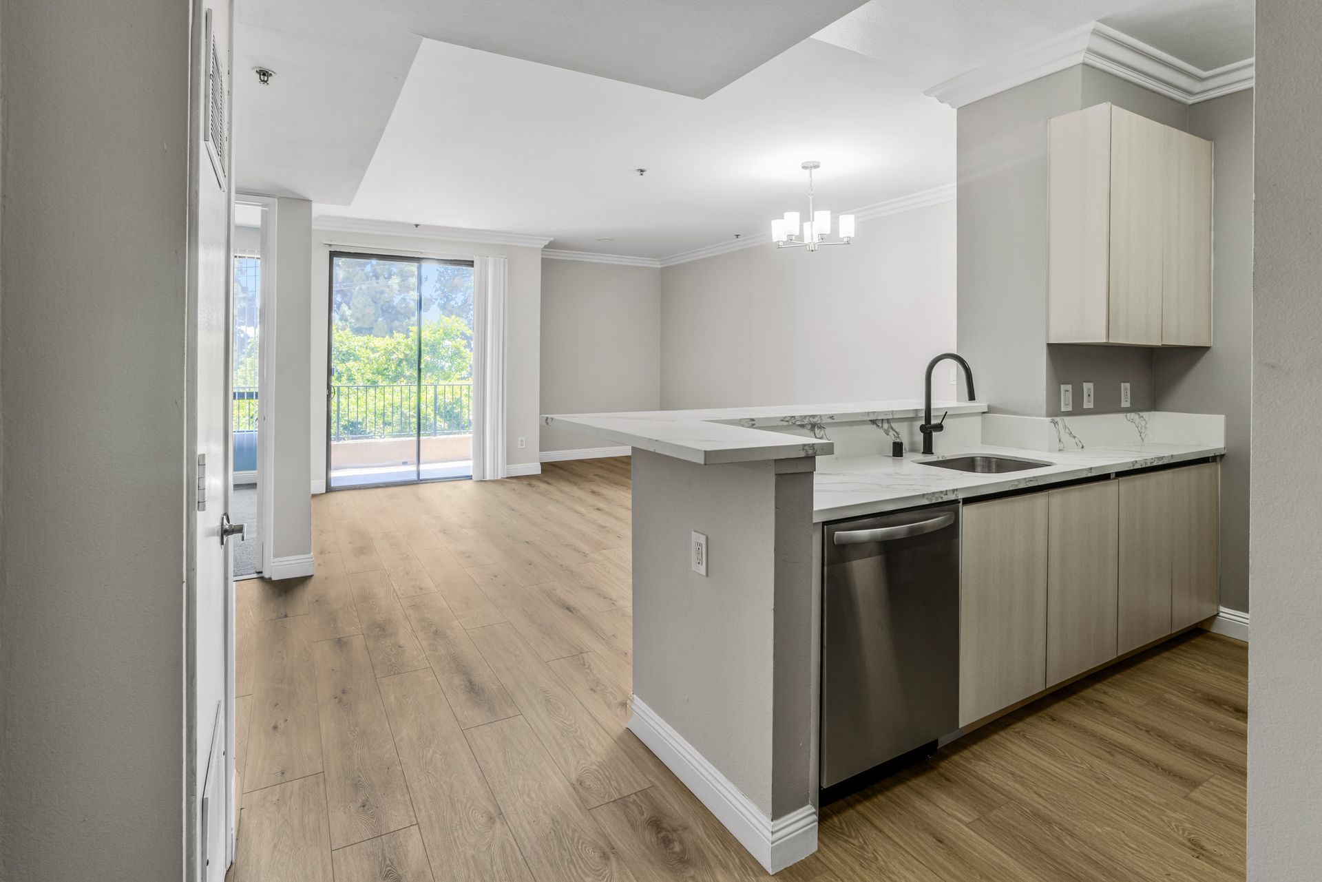 Bright modern kitchen with white cabinets, island, stainless dishwasher, and sliding glass doors to a balcony