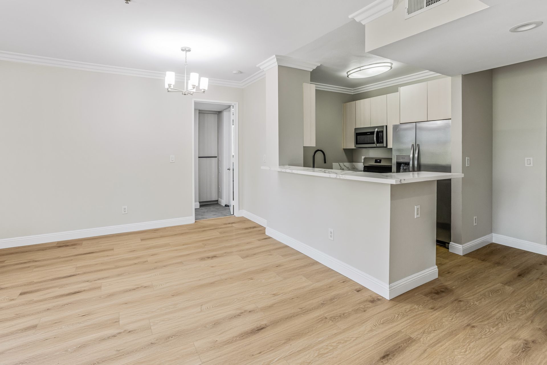 Empty open-plan living room with light wood floors and a white kitchen pass-through counter