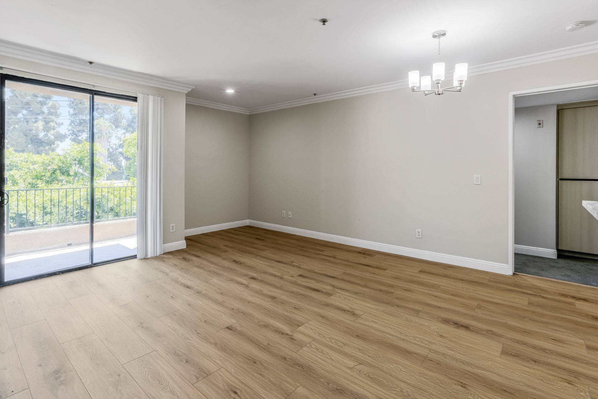 Empty modern living room with wood floors, sliding glass doors, and neutral walls with chandelier lighting