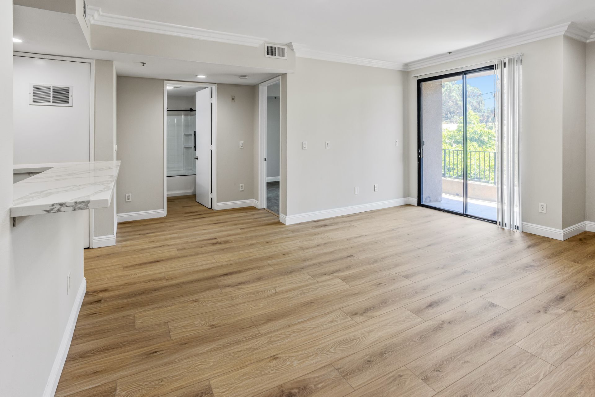 Empty bright living room with light wood floors, white walls, fireplace, and sliding glass doors to a balcony
