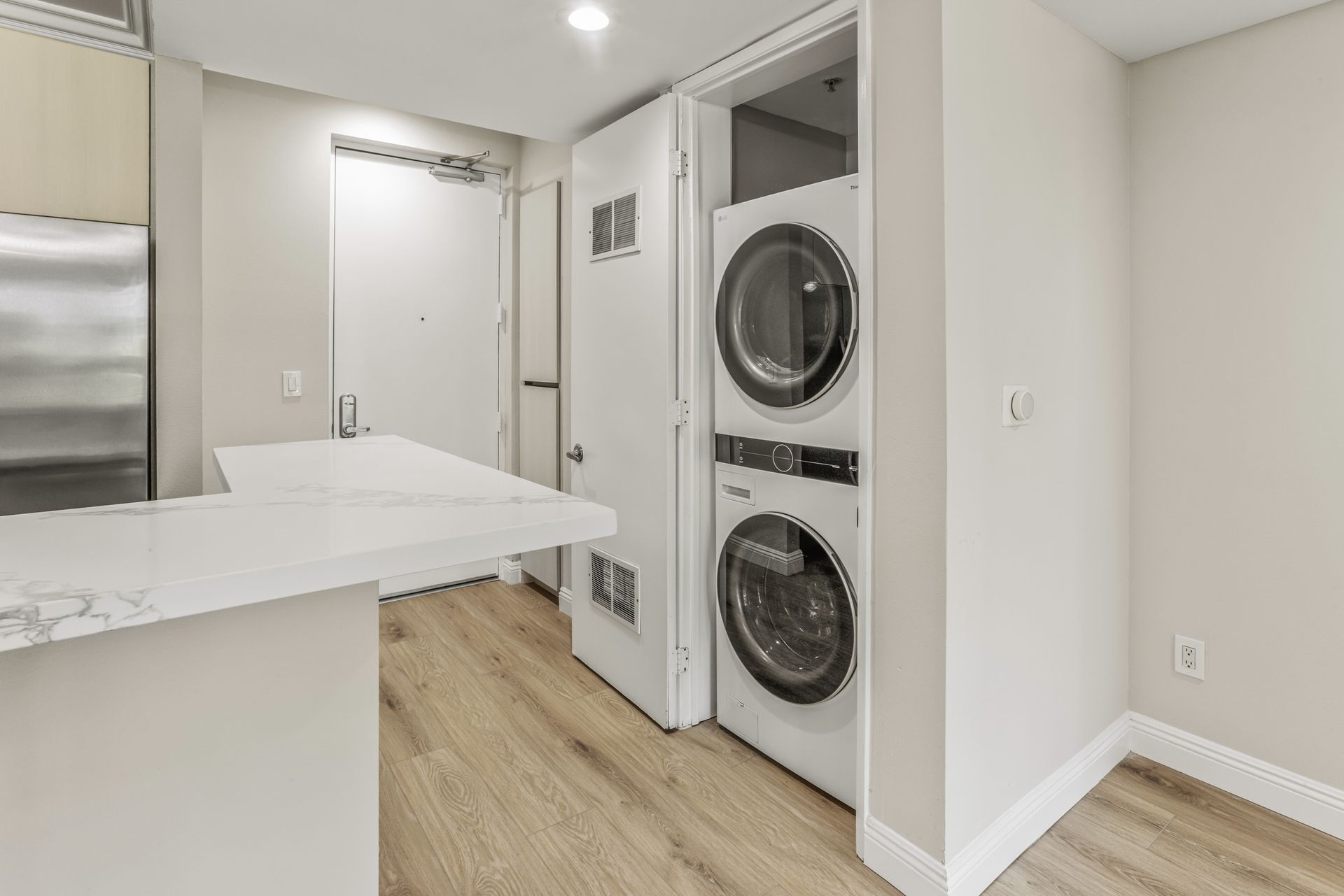 Bright laundry room with stacked washer and dryer, white cabinets, and light wood floor