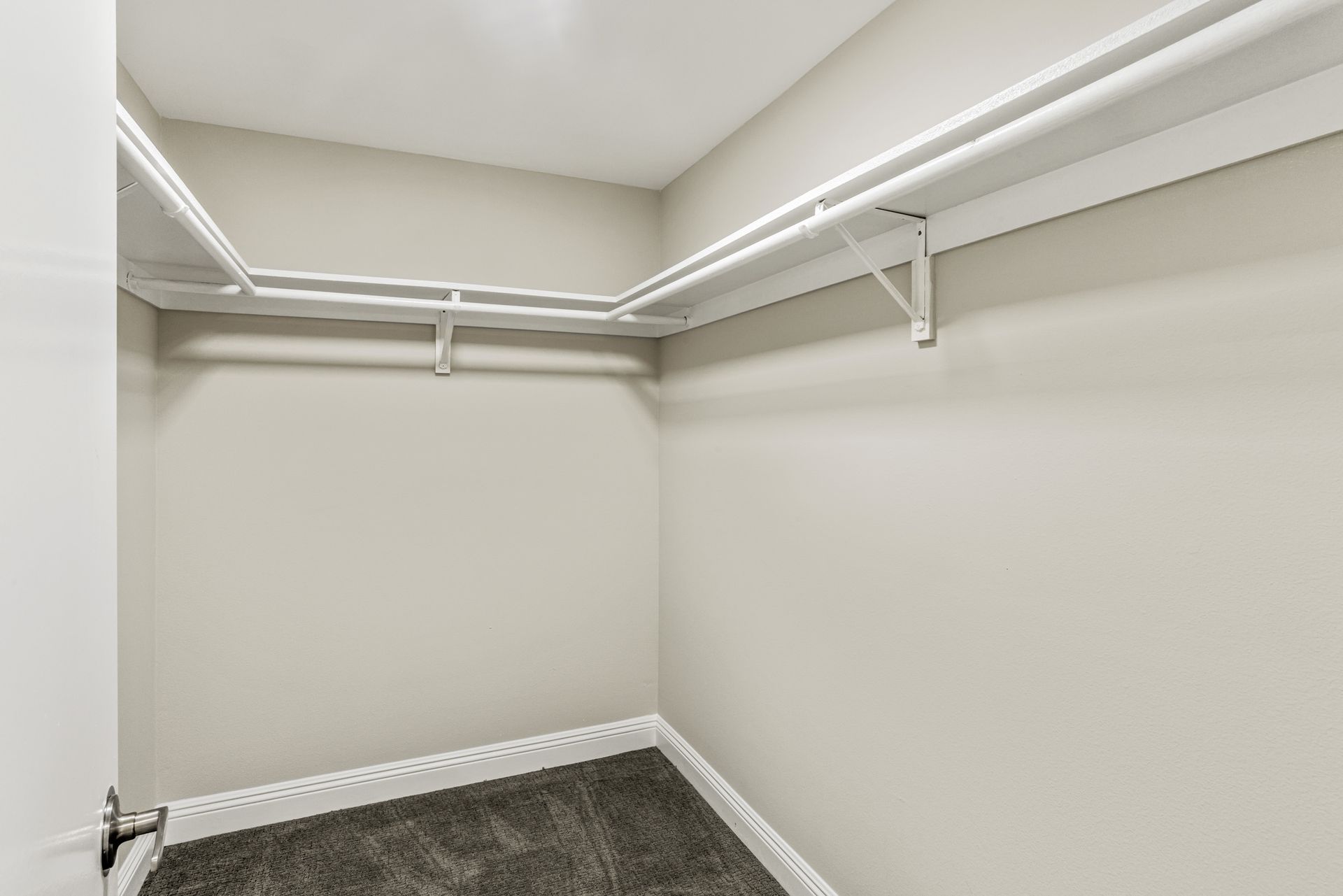 Empty walk-in closet with white walls, wire shelving, and gray carpet flooring.