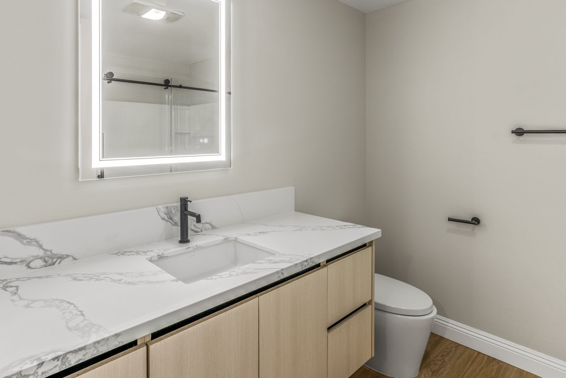 Modern bathroom vanity with white countertop, black faucet, mirror, and toilet in a neutral-toned room