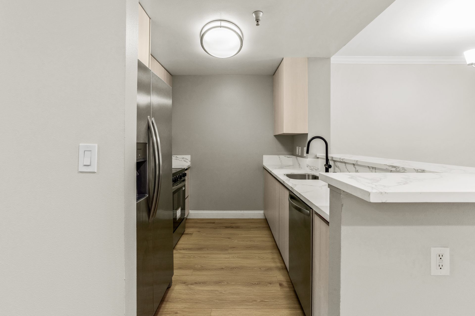 Modern kitchen with stainless steel refrigerator, white counters, and wood flooring