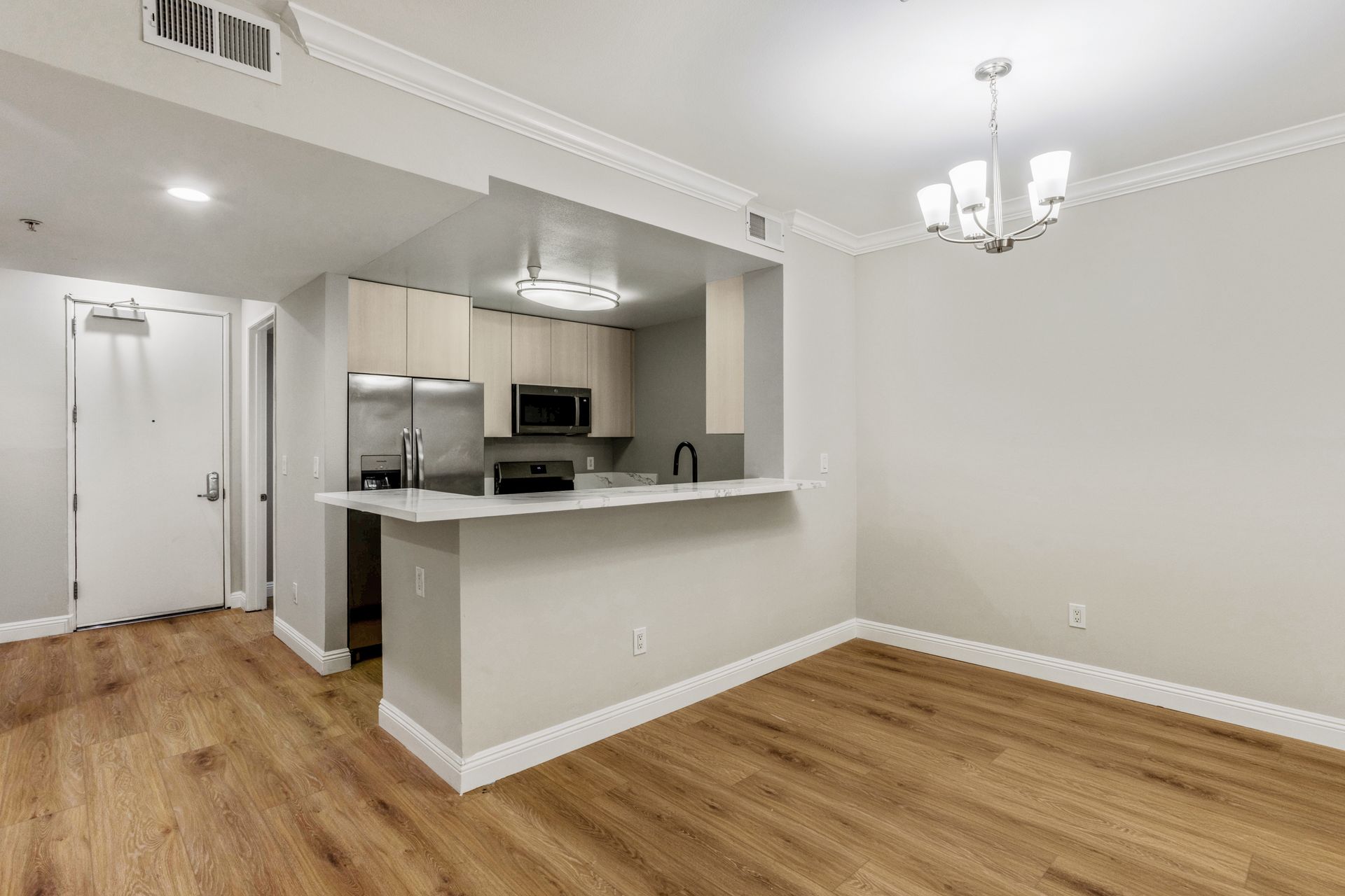 Empty open-plan kitchen and dining area with white walls, hardwood floors, and a breakfast bar.