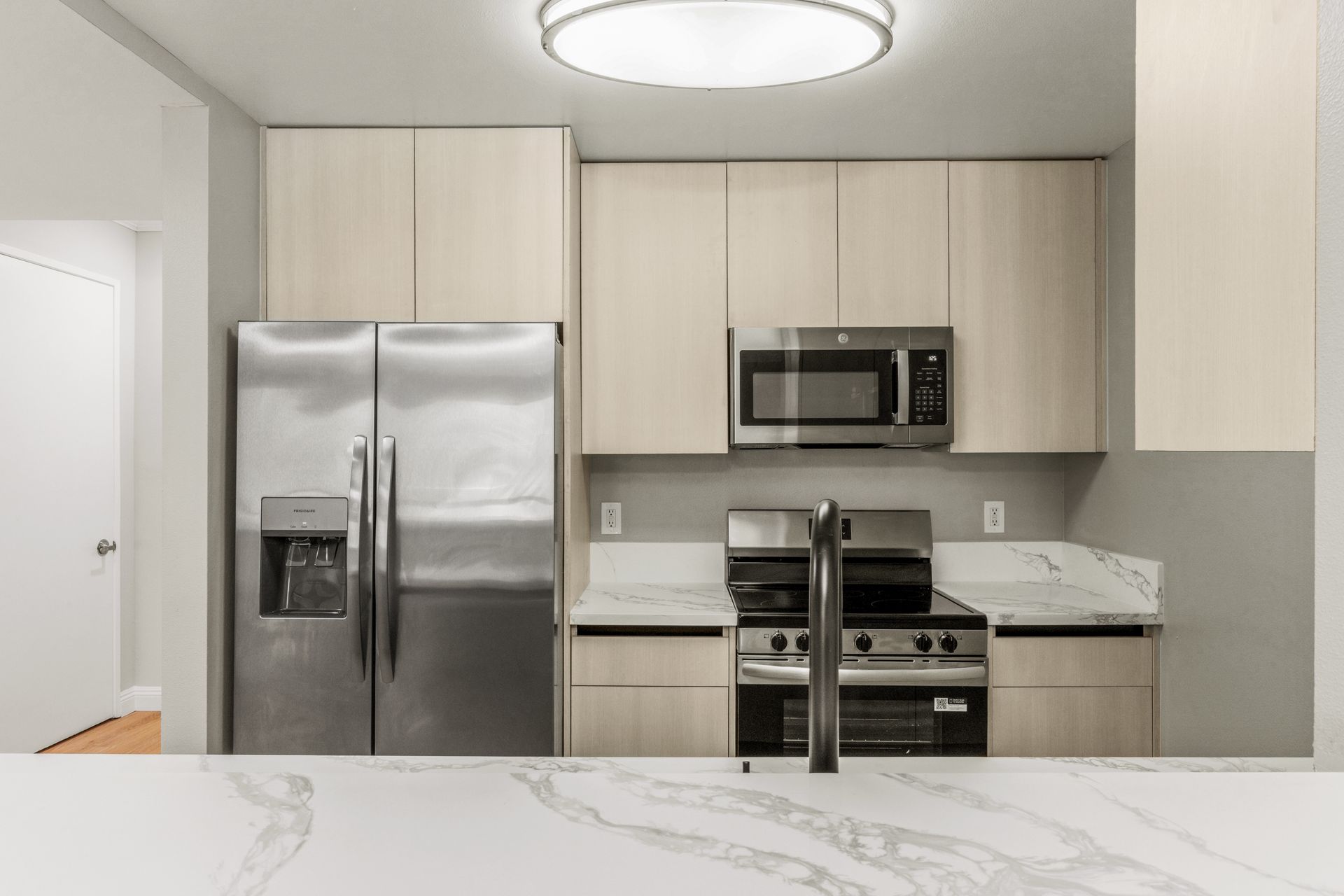 Modern kitchen with stainless steel appliances, light wood cabinets, and marble island countertop.