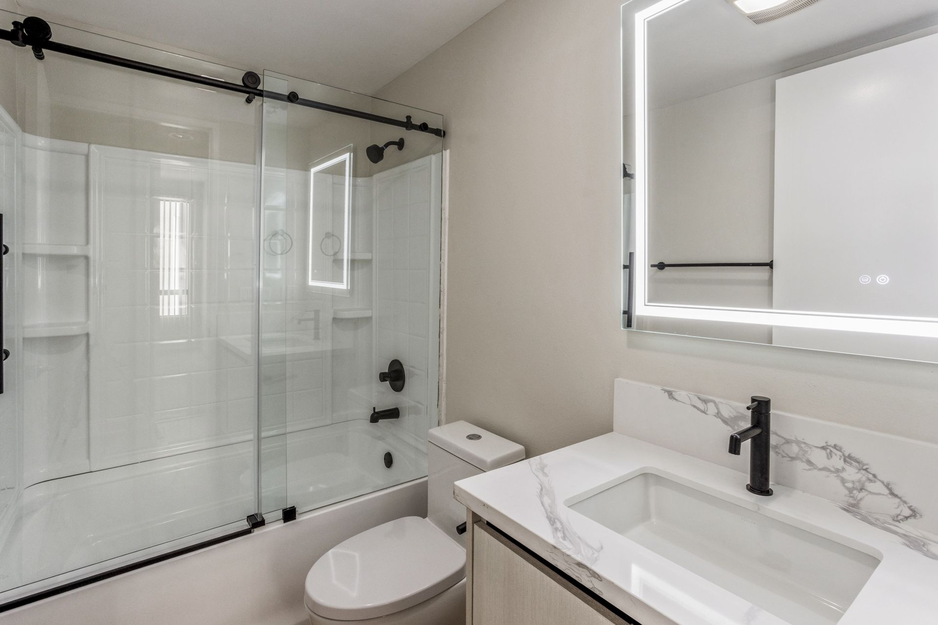 Modern bathroom with glass shower, toilet, and white vanity with illuminated mirror