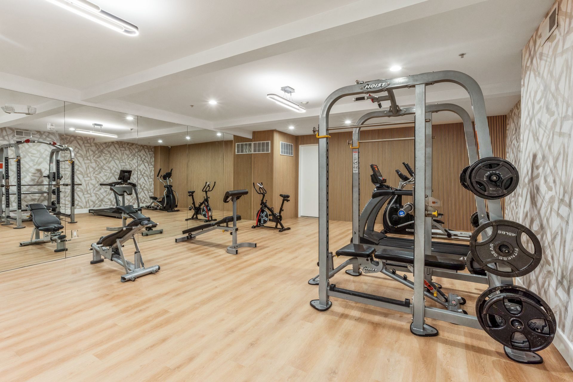 Bright gym with workout machines, weights, and mirrors on light wood floors