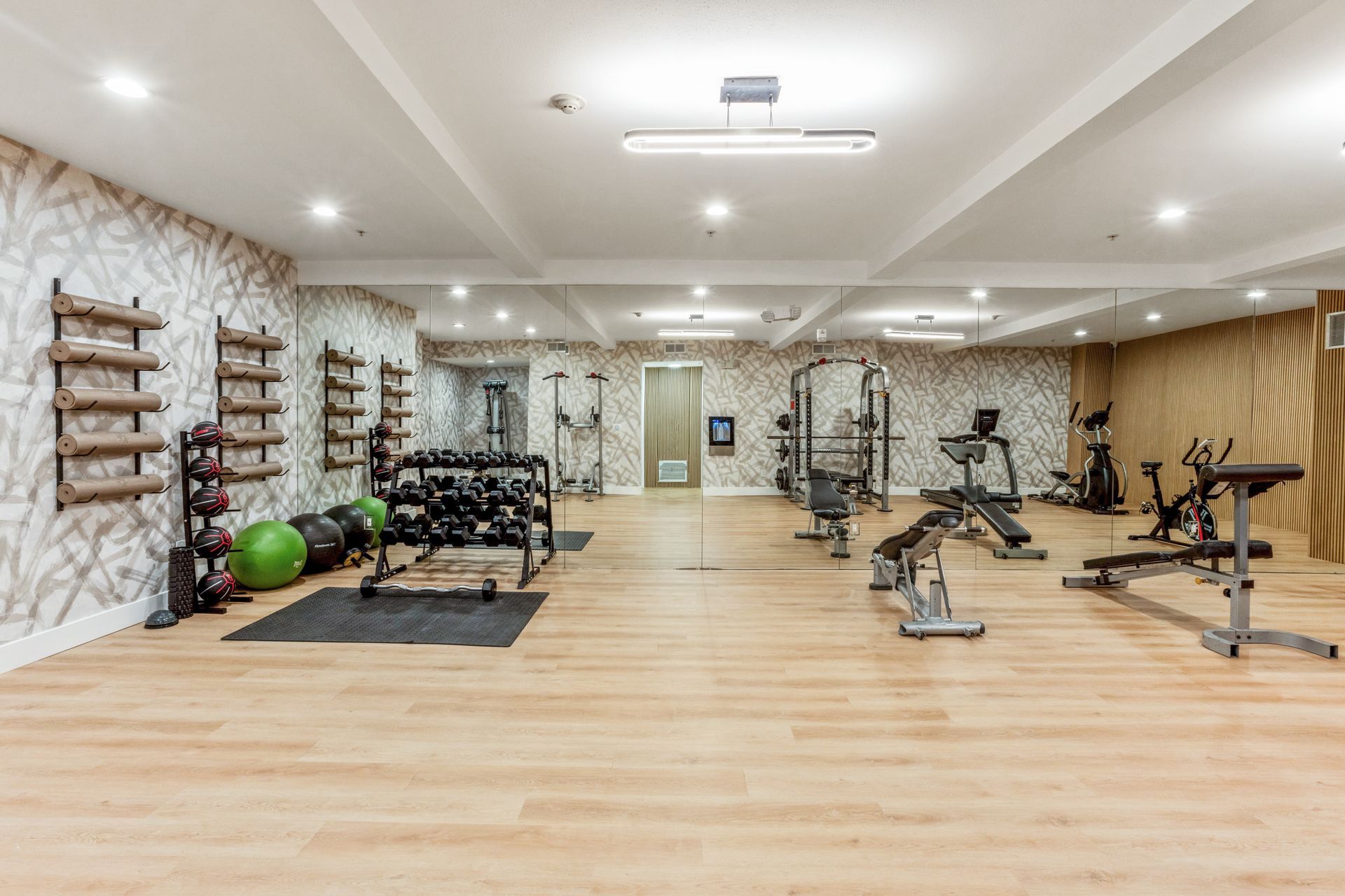 Spacious home gym with weight machines, benches, dumbbells, mirrors, and a wooden floor