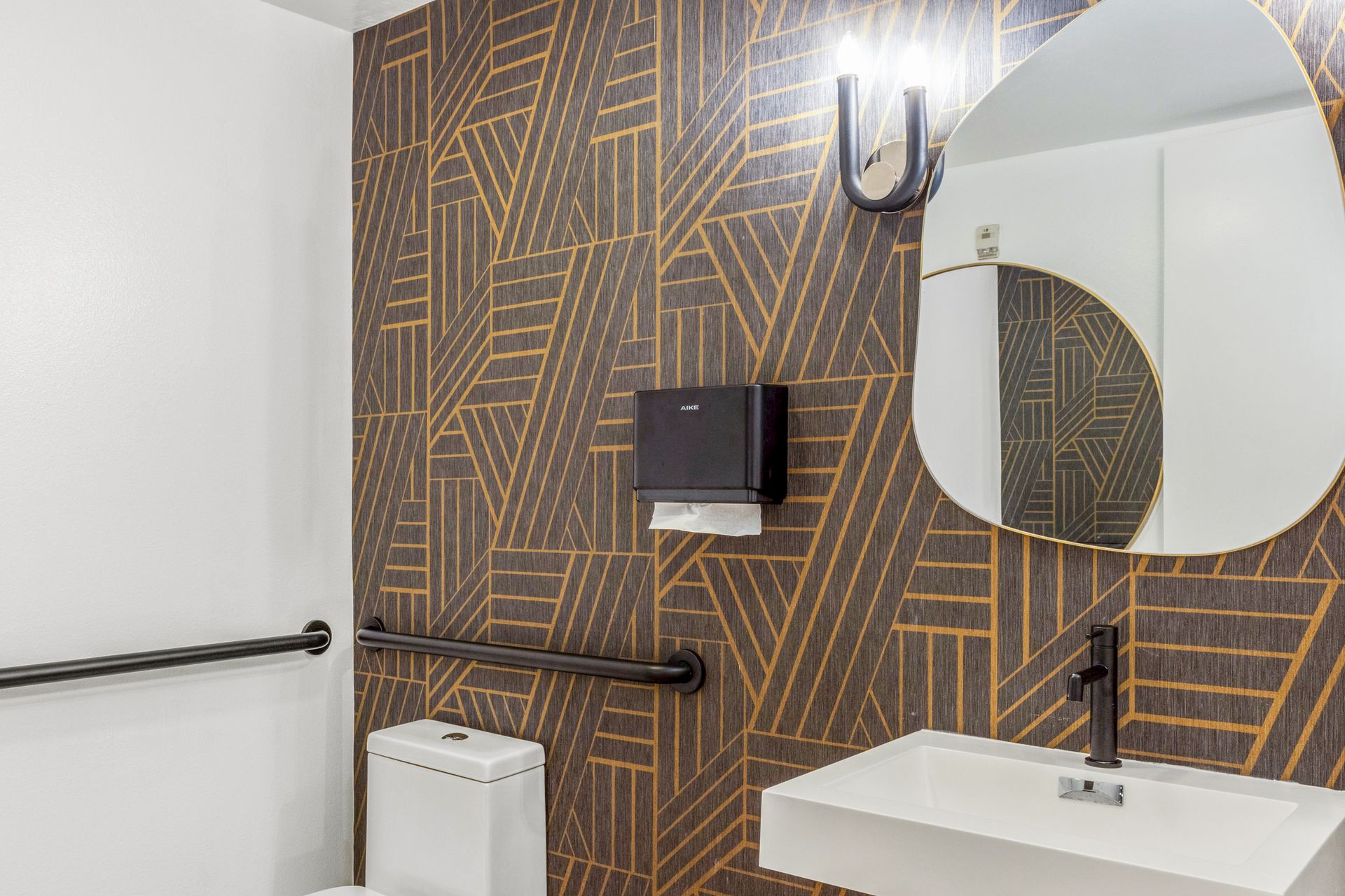 Modern bathroom with patterned accent wall, round mirror, sink, and toilet